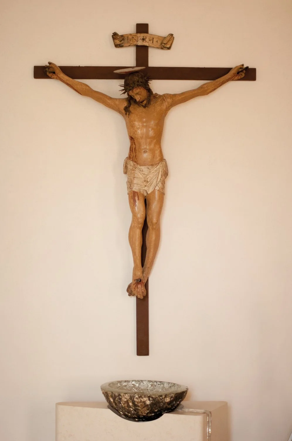 A crucifix with a detailed sculpture of Jesus Christ hanging on a wooden cross, with a skull-shaped chalice positioned below.