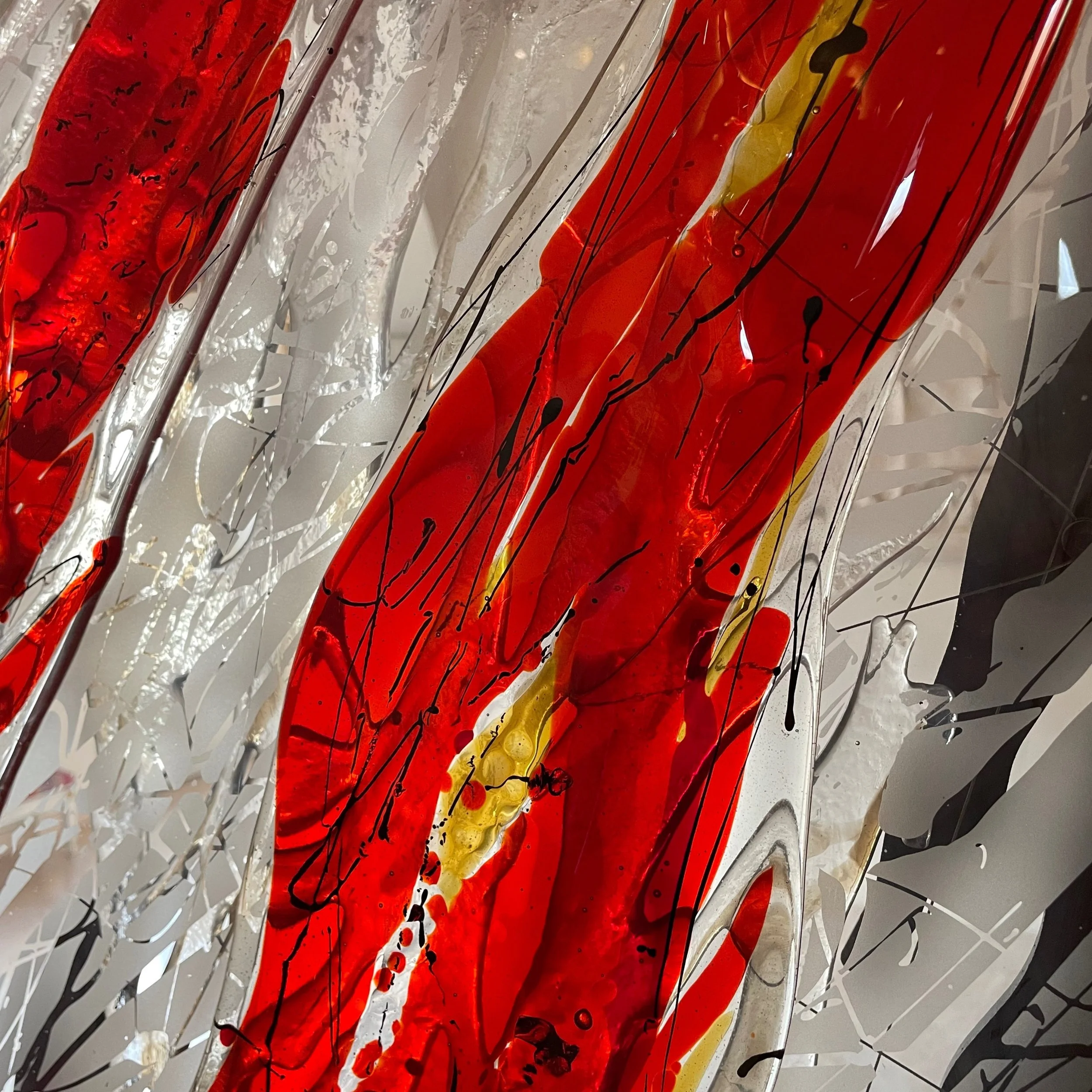 Close-up of an abstract expressionist painting featuring bold red, yellow, white, black, and gray colors with splatters and drips.