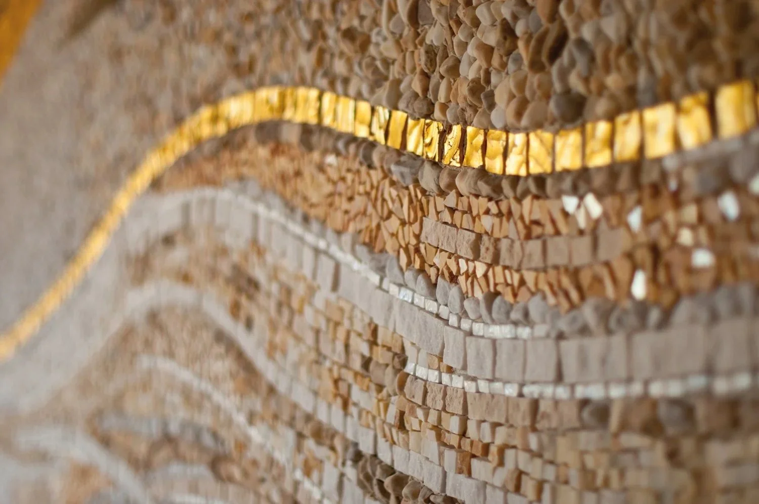 Close-up of a wall mosaic made of small, irregularly shaped stones and a strip of yellow gold-colored tiles.