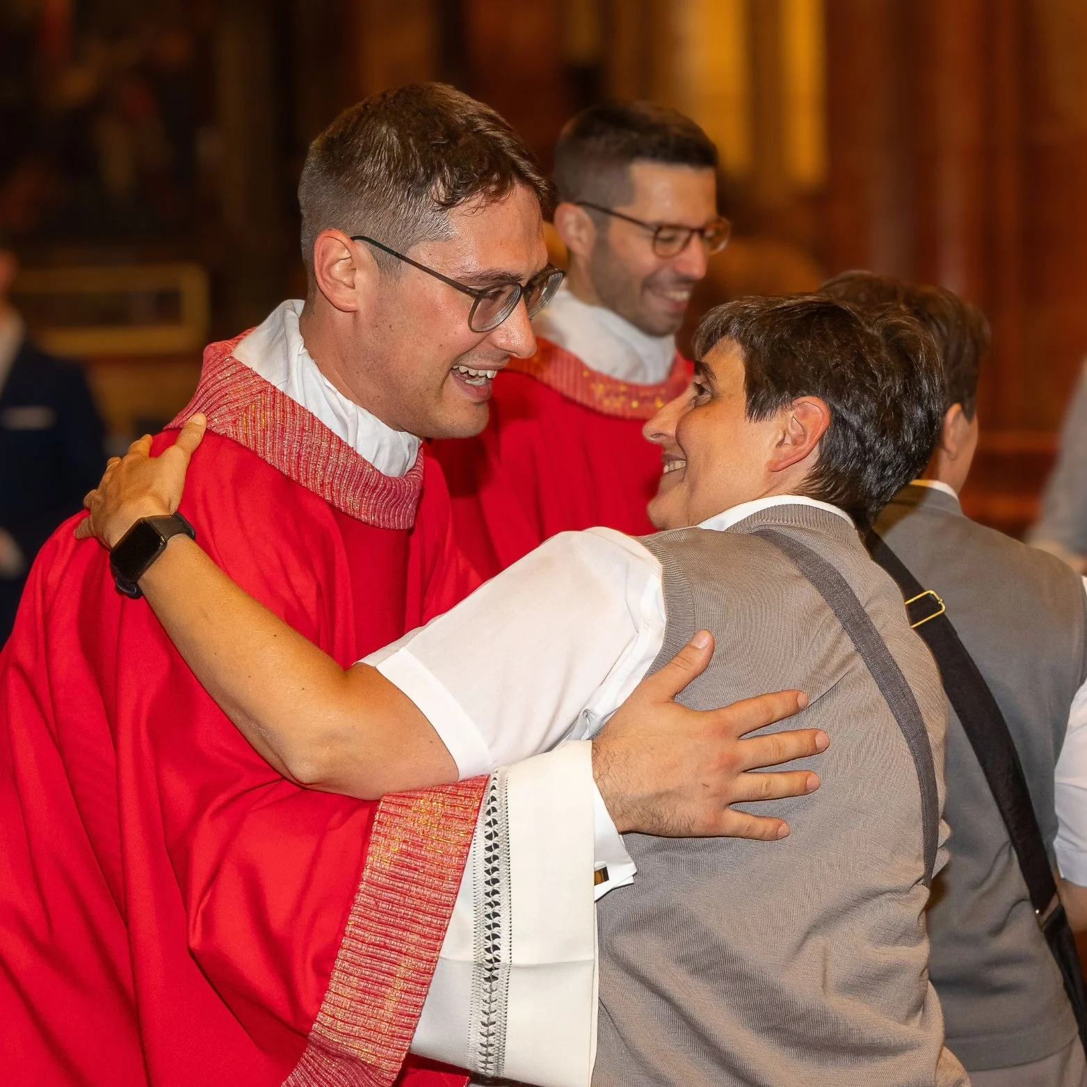 A group of people happily hugging each other, one person wearing gowns, in a warmly lit room.