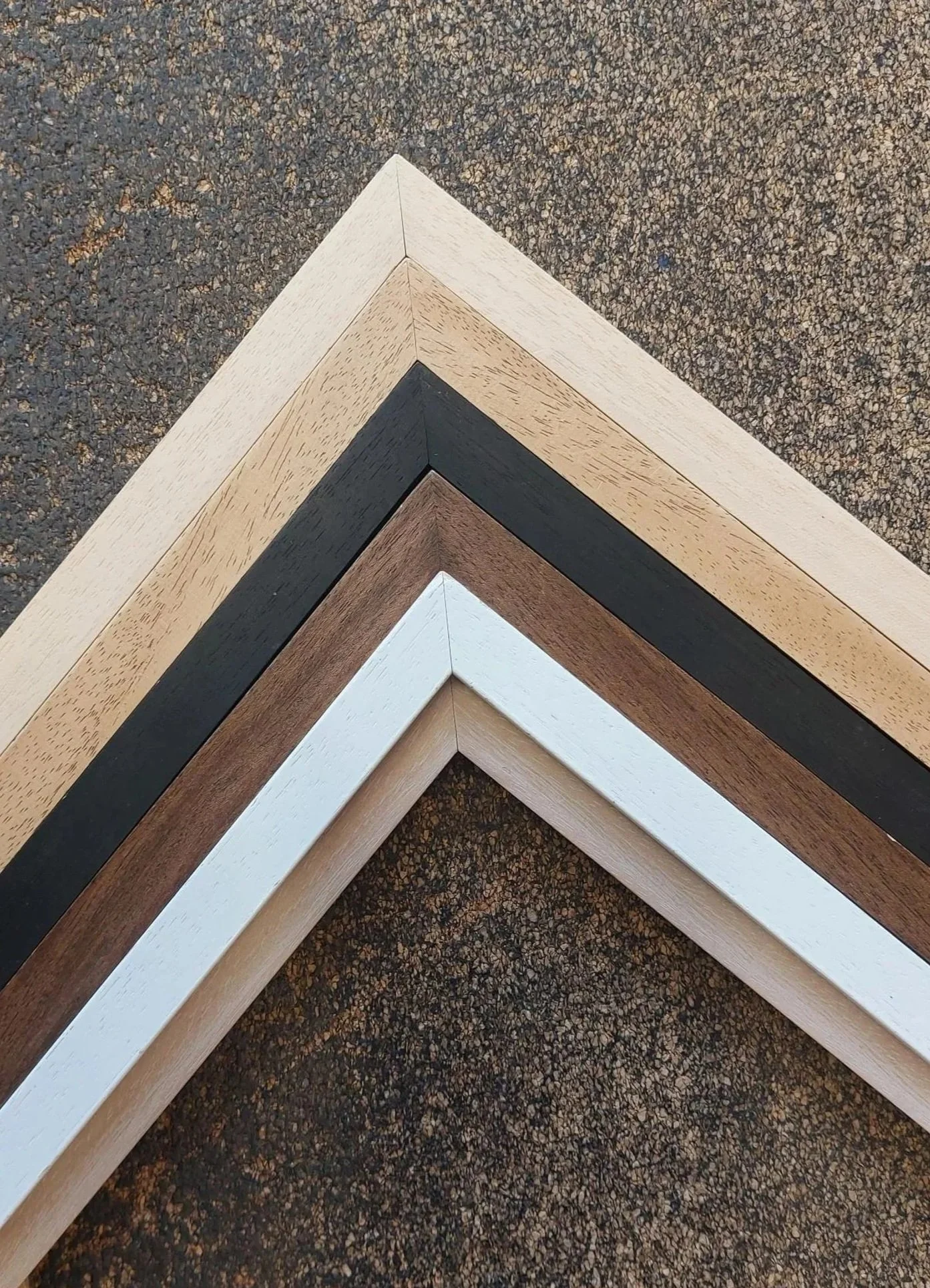 Close-up of four wooden picture frames, each painted in different colors, arranged in a layered V-shape on a textured surface.