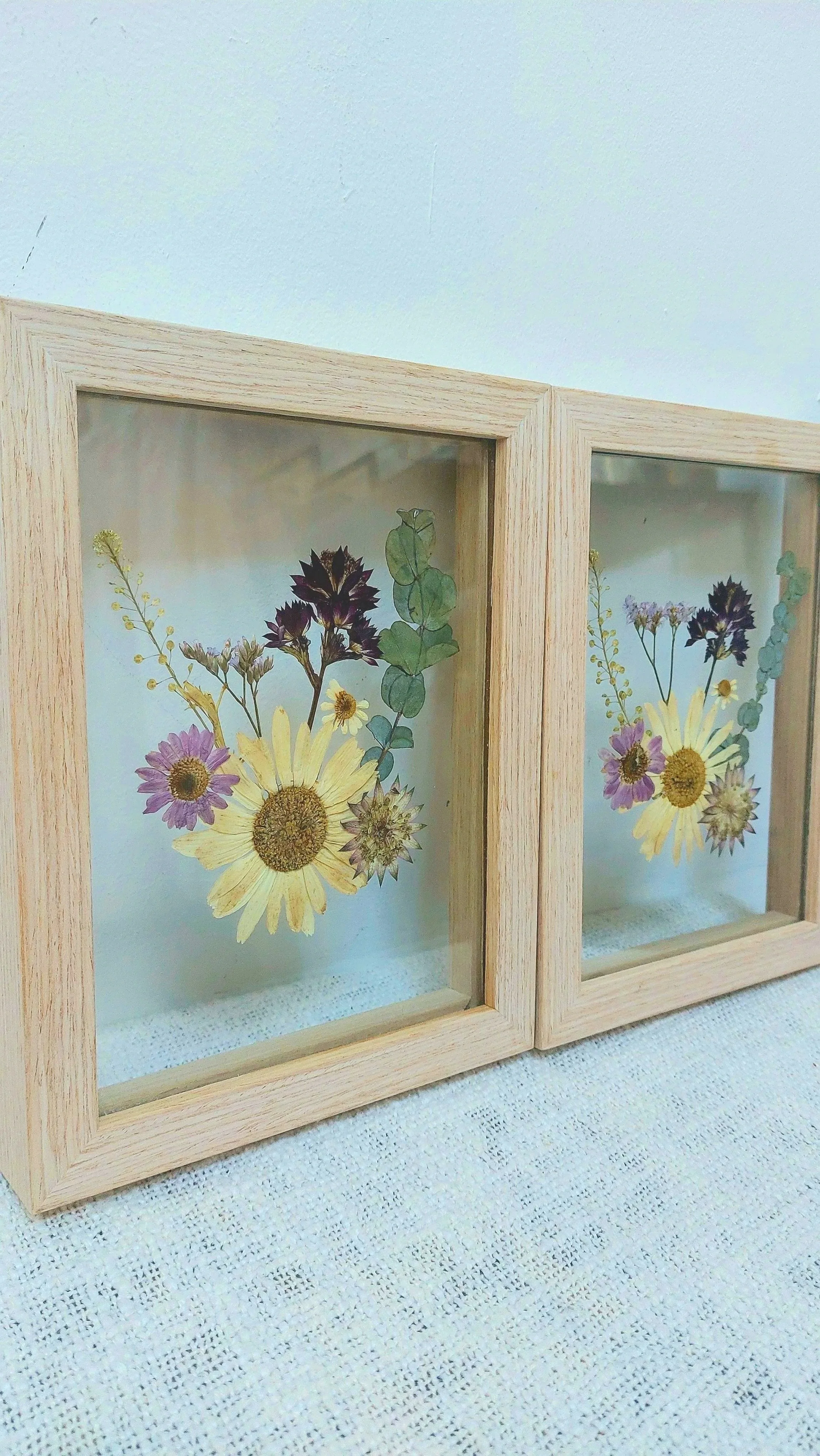 Two wooden shadow boxes with pressed dried flowers inside, arranged in a floral pattern.