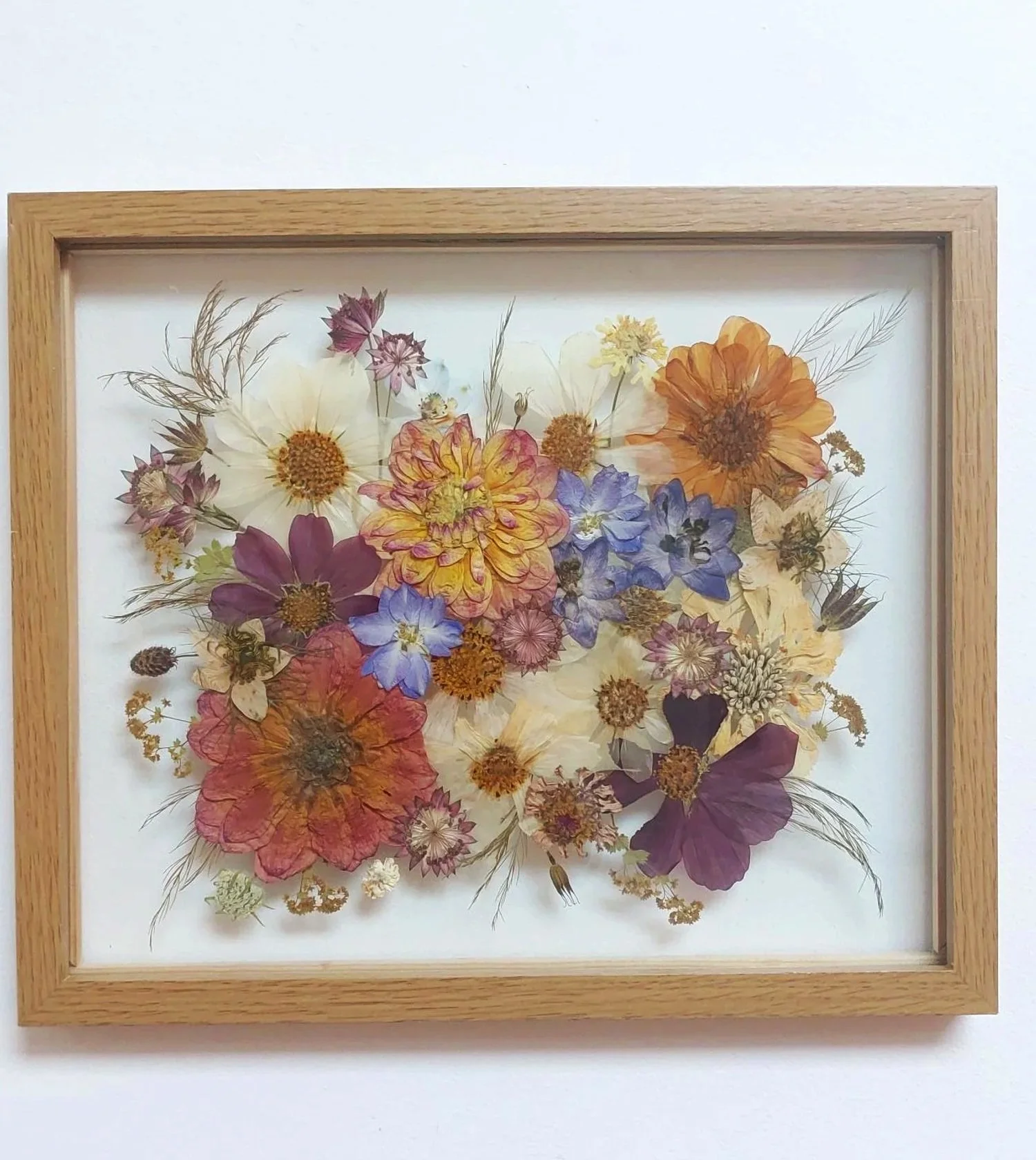 Framed wall art made of pressed and dried colorful flowers arranged artistically.