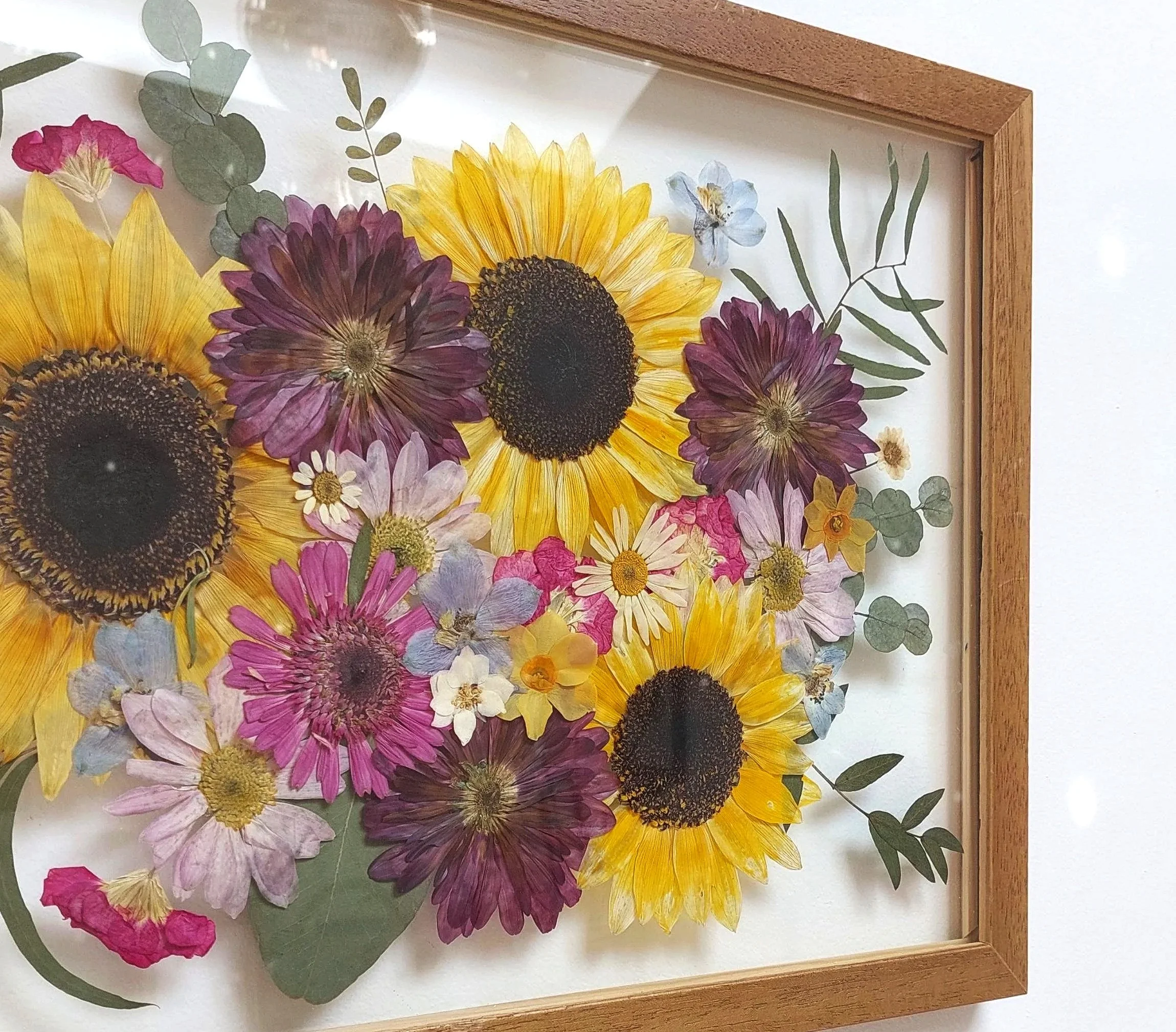 Pressed flower artwork featuring sunflowers, daisies, and other colorful flowers in a wooden frame.