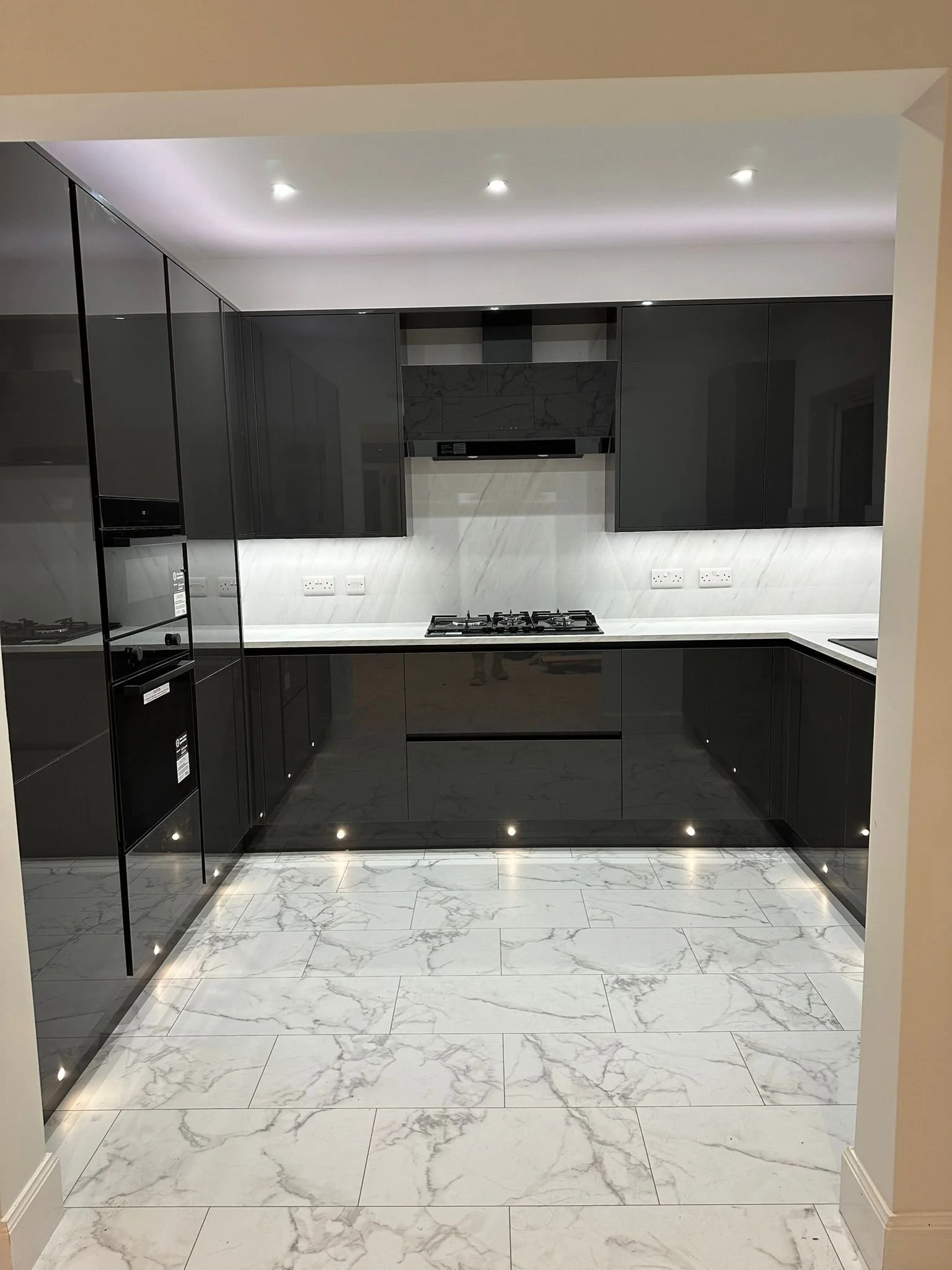 Modern black kitchen with marble countertops, black cabinets, built-in oven, gas cooker, and white marble tiled floor with gray veining.
