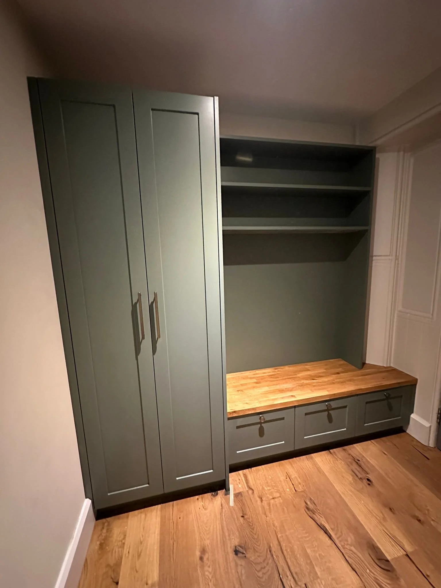 A wall-mounted storage unit with cabinets, open shelves, and a wooden bench with drawers underneath.