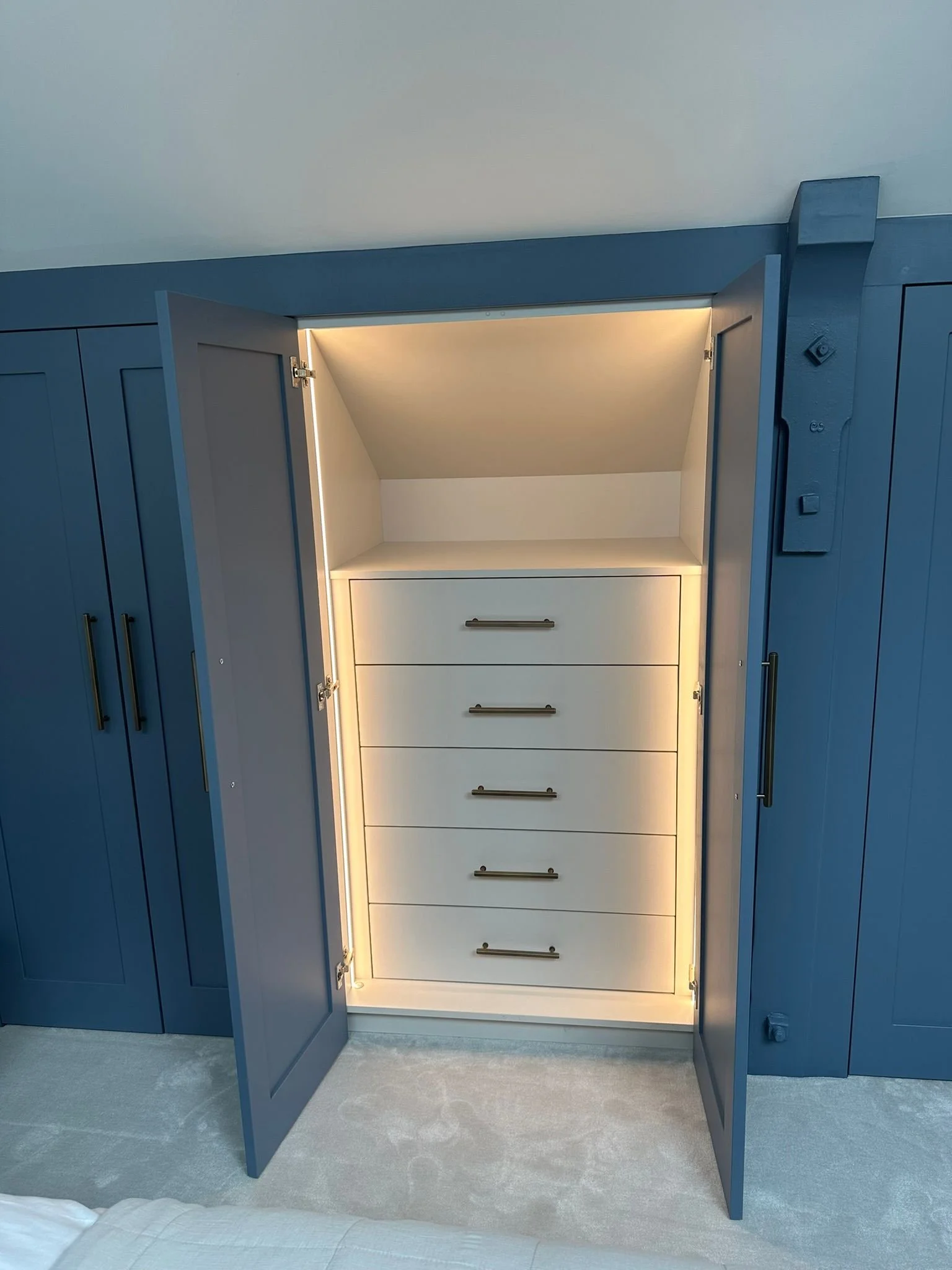 Open blue wardrobe with built-in lighting reveals white drawers inside.