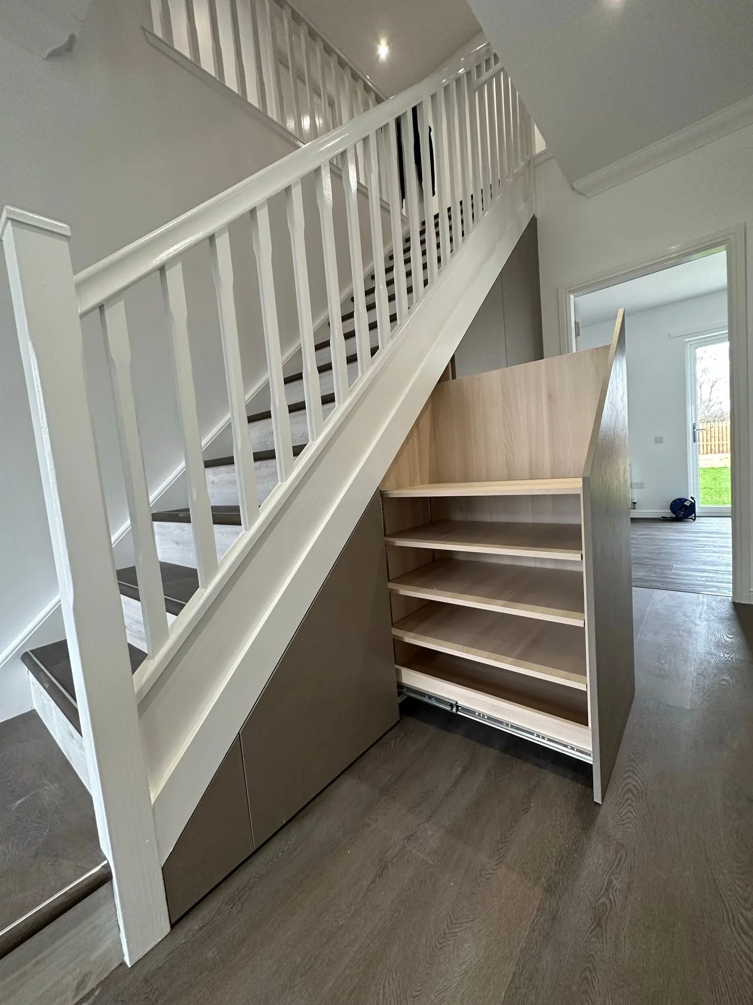 Unfinished staircase with a white railing and a partially built wooden storage unit underneath, in a modern home interior.