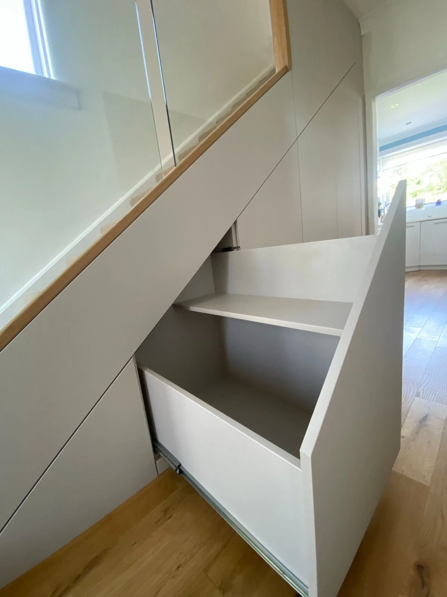 Built-in storage drawer with a slide-out shelf beneath a staircase in a modern kitchen.