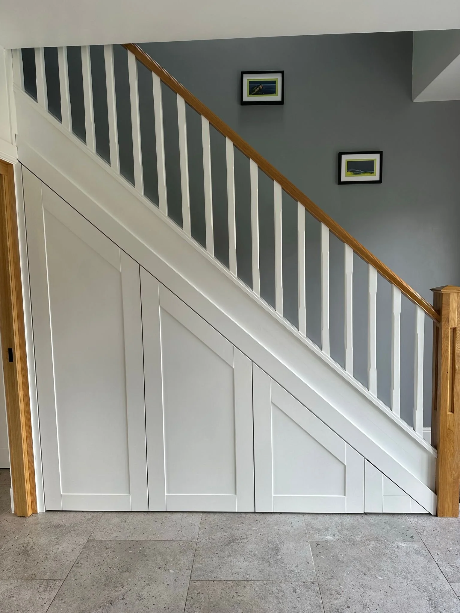 Interior staircase with white paneling on the lower half and a blue wall with two framed pictures above.