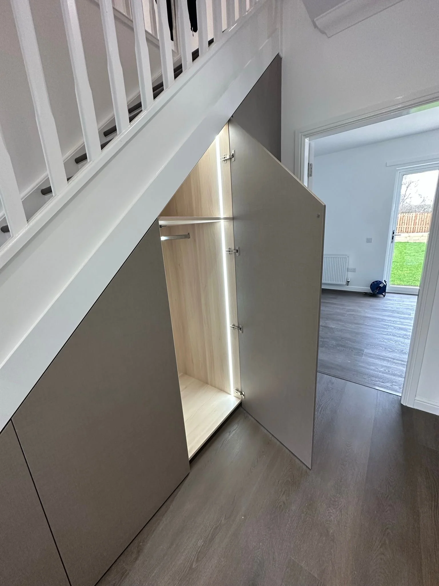 Open built-in shoe storage cabinet under staircase in a modern home with white walls and hardwood flooring.