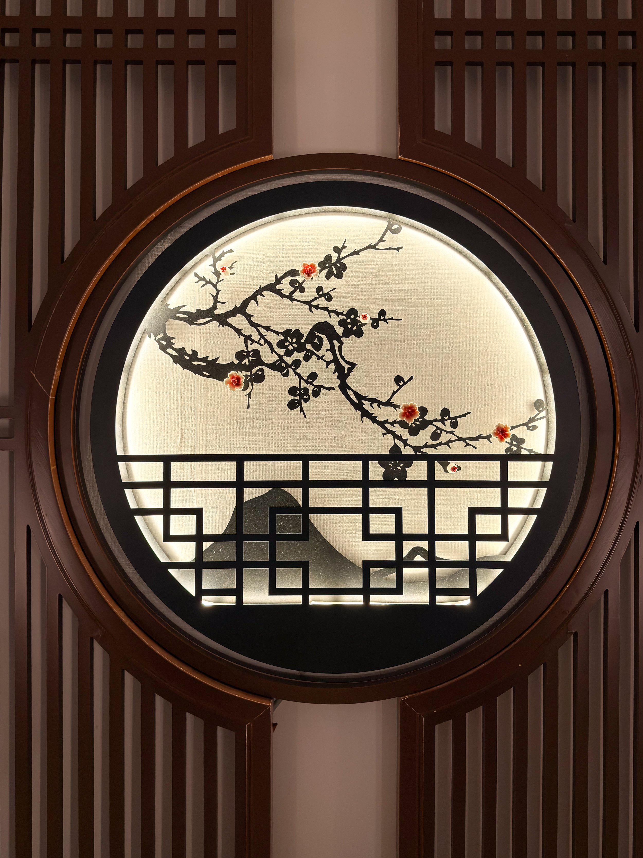 Decorative circular wall art with a black cherry blossom branch, red flowers, and a stylized mountain, framed by wooden slats.