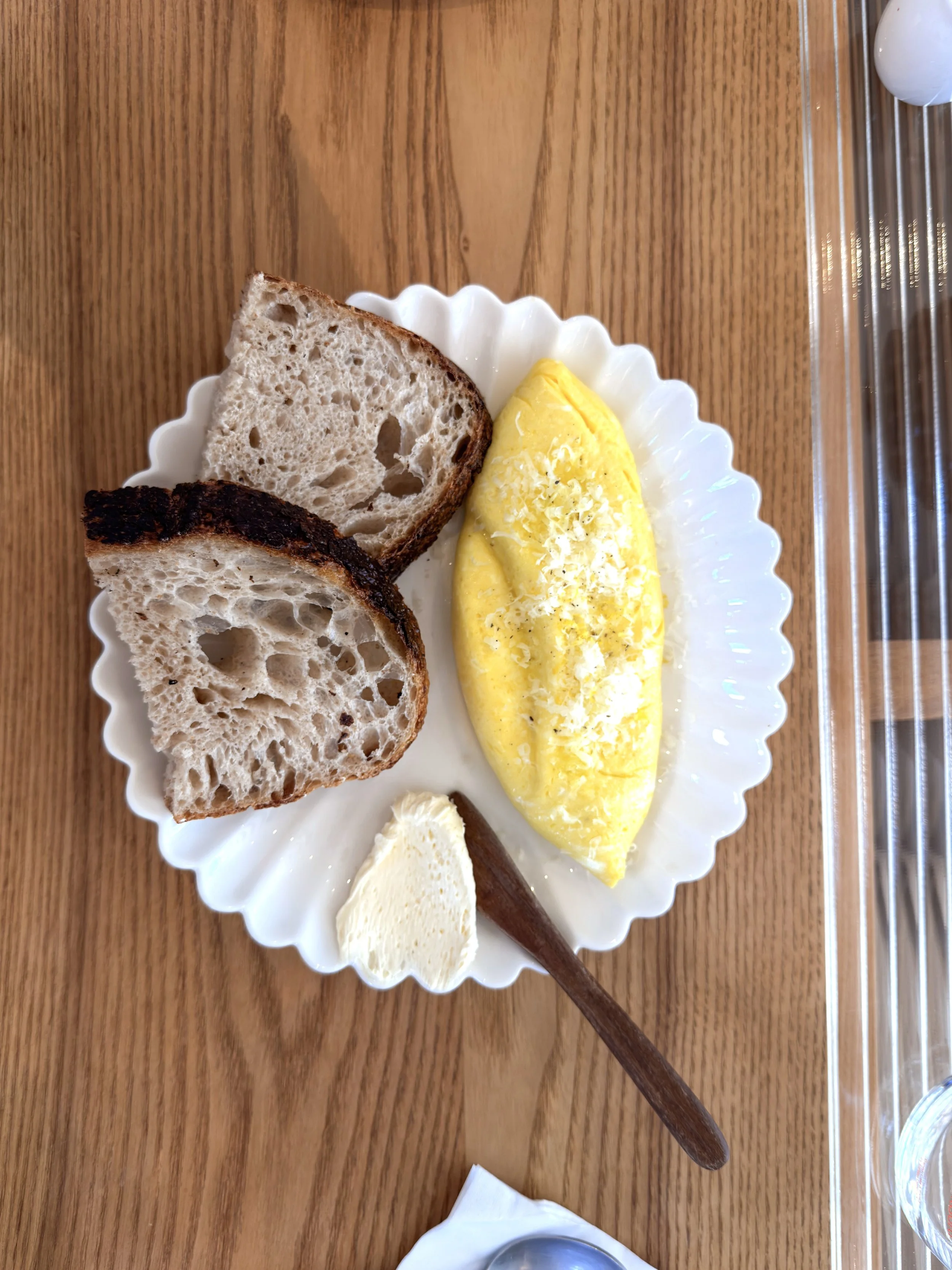 Plate with scrambled eggs topped with cheese, two slices of toasted bread, a pat of butter, and a cinnamon stick on a wooden table.
