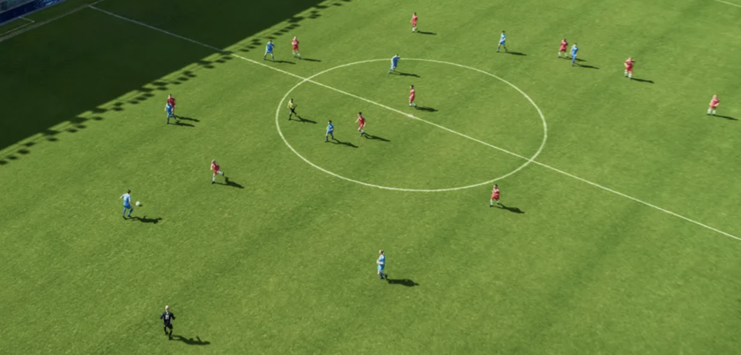 Soccer match with players in red and blue uniforms on a green field, shadow of stadium structure on the ground.