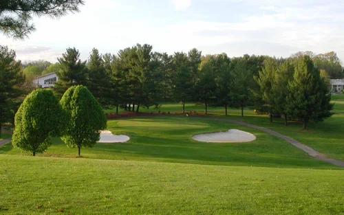 A scenic view of a golf course with green grass, two sand bunkers, and numerous trees in the background.