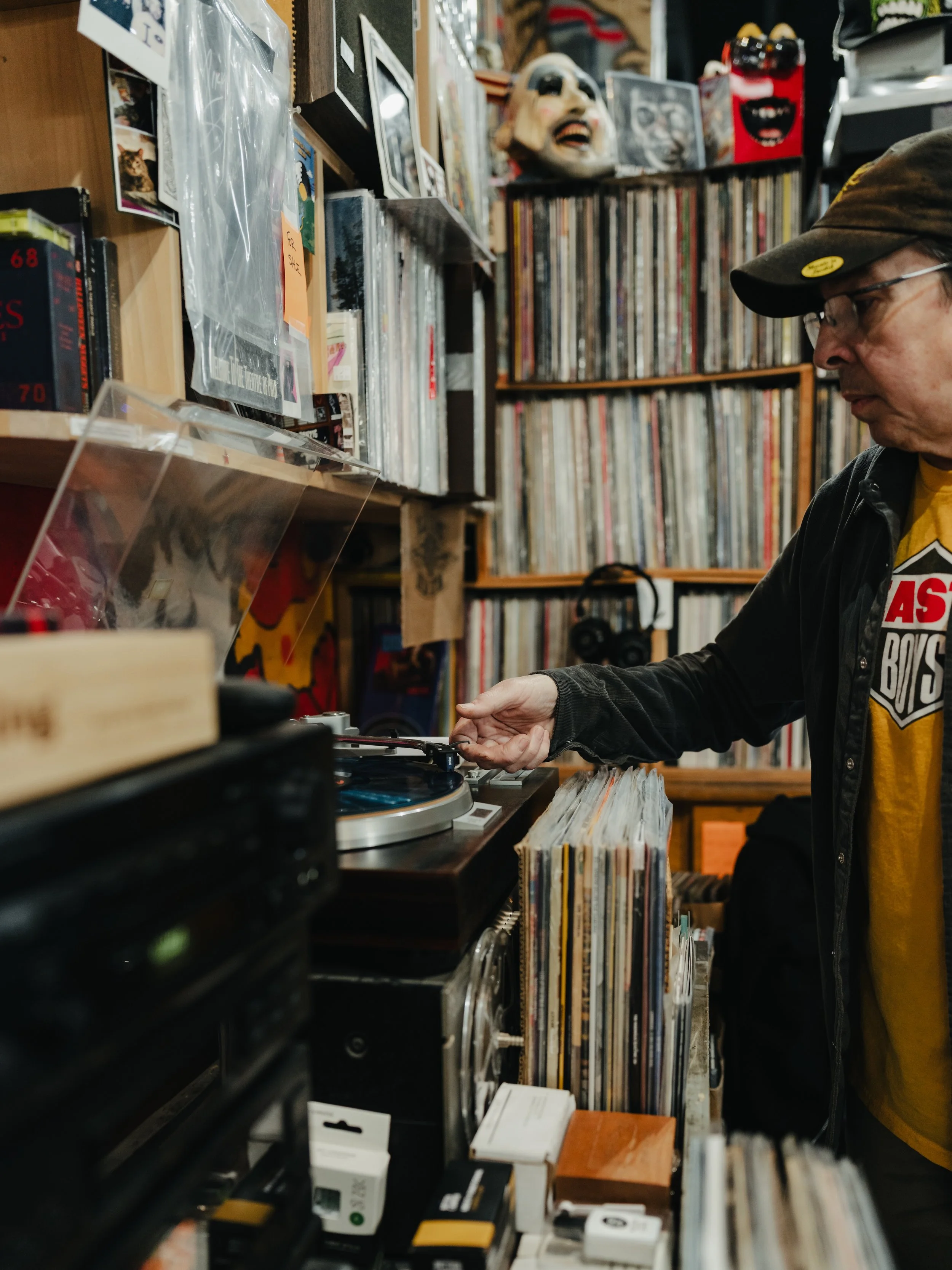 A man browsing vinyl records at a record store, surrounded by shelves filled with records and collectibles.