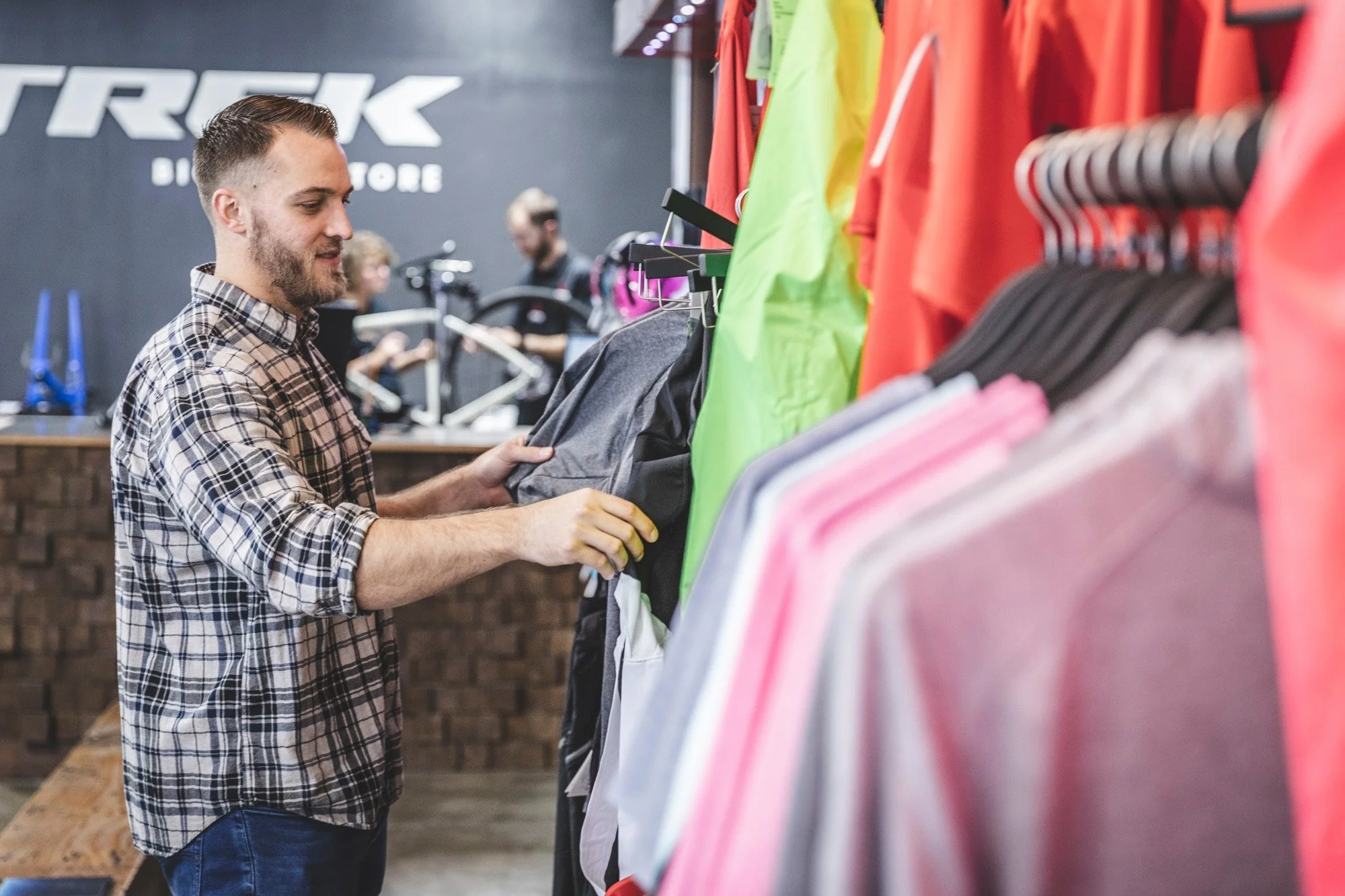 A man shopping for clothes in a store with cycling gear, browsing through colorful jackets and shirts on a rack.