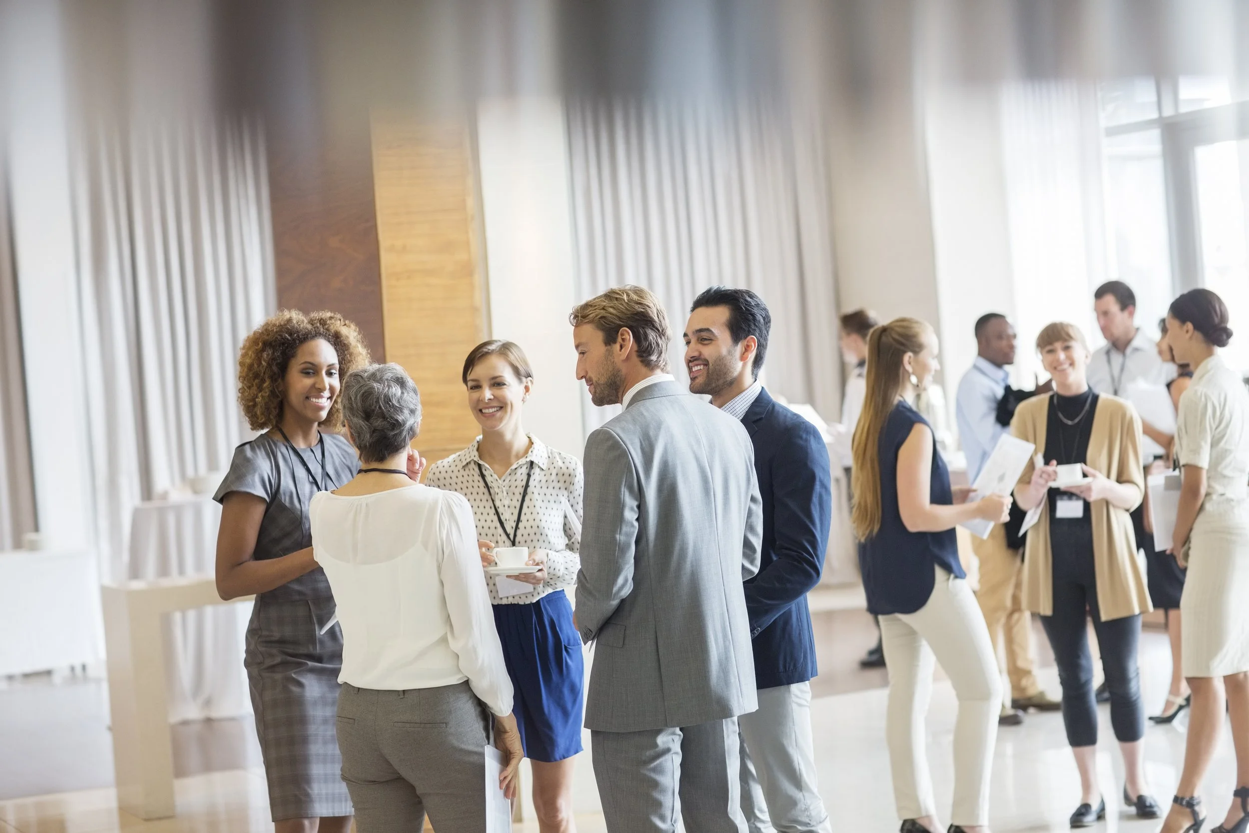 Business professionals and conference attendees talking and networking in a well-lit, modern indoor space during a professional event.