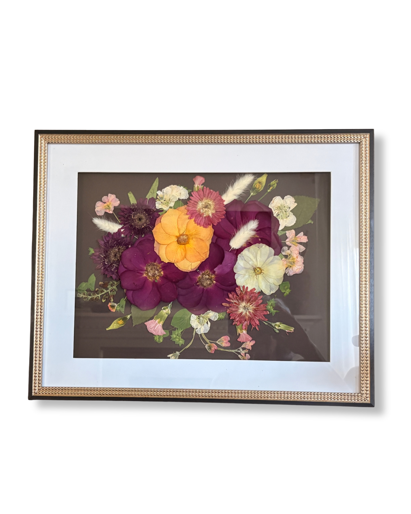Framed pressed flower art with various purple, yellow, white, and pink flowers and green leaves on a dark background.
