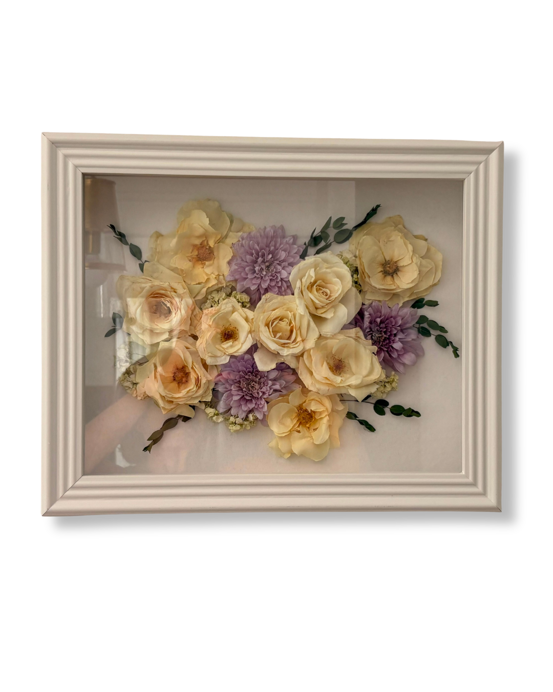 Framed display of cream-colored roses and purple dahlias arranged on a white background.