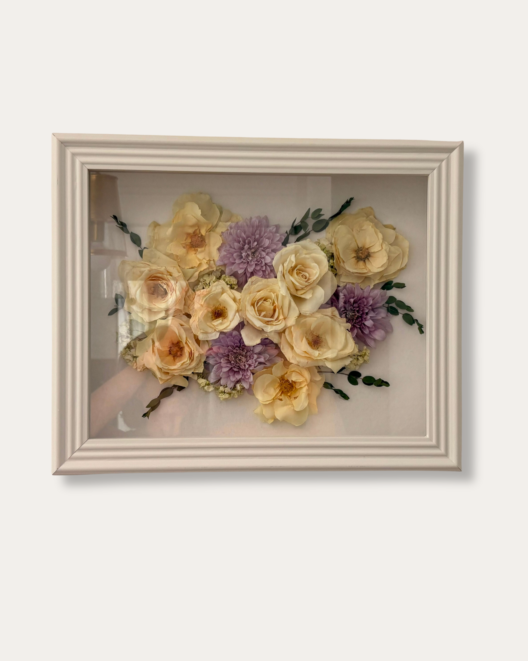A framed floral arrangement featuring cream roses and purple dahlias on a white background.