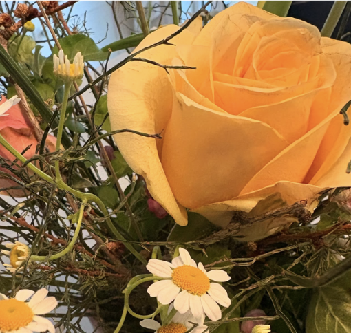 A bouquet featuring a large peach-colored rose, small white daisies with yellow centers, and green foliage.