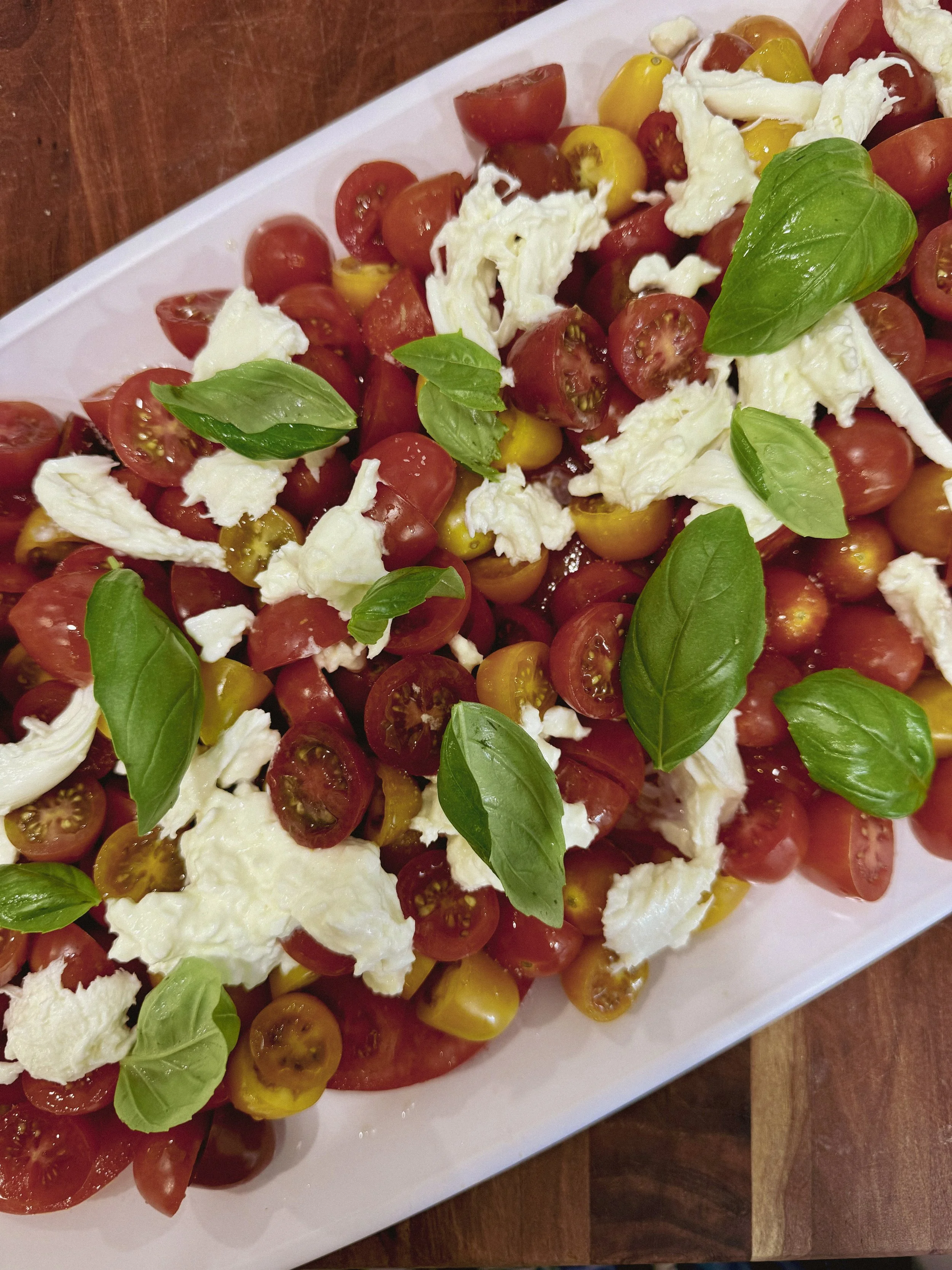 Caprese salad with cherry tomatoes, fresh mozzarella, and basil leaves on a white platter.