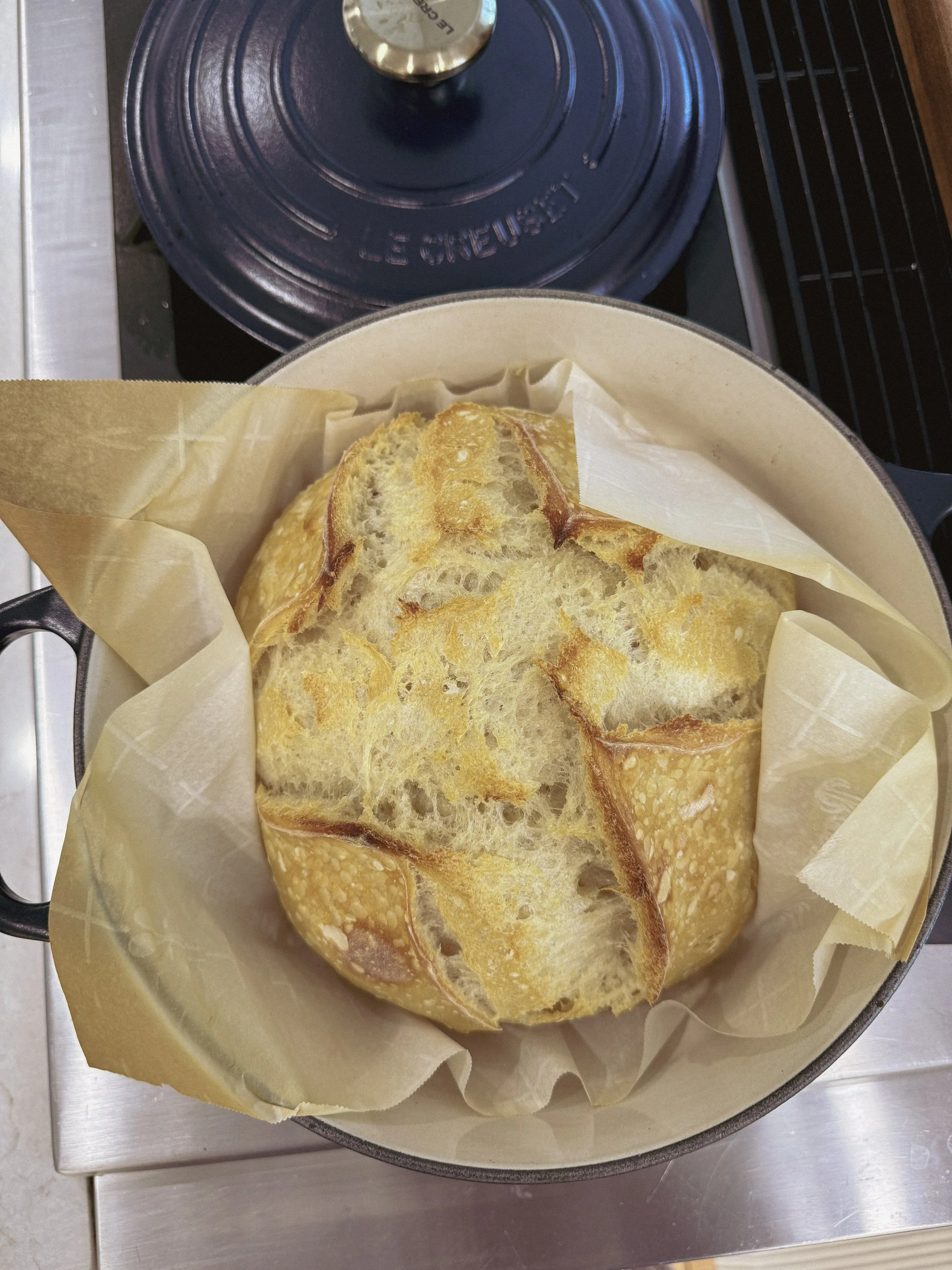 A round loaf of bread in a pot lined with parchment paper on a stove.