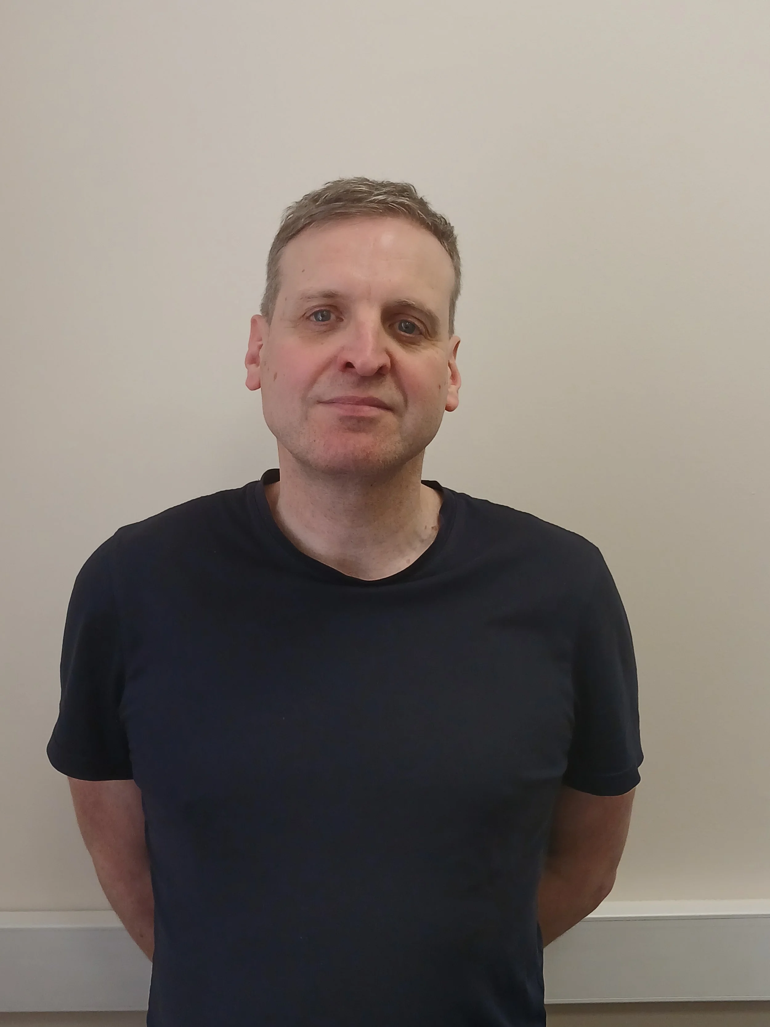 A woman sitting on a bench in a minimalist room, with sunlight casting shadows on the wall.