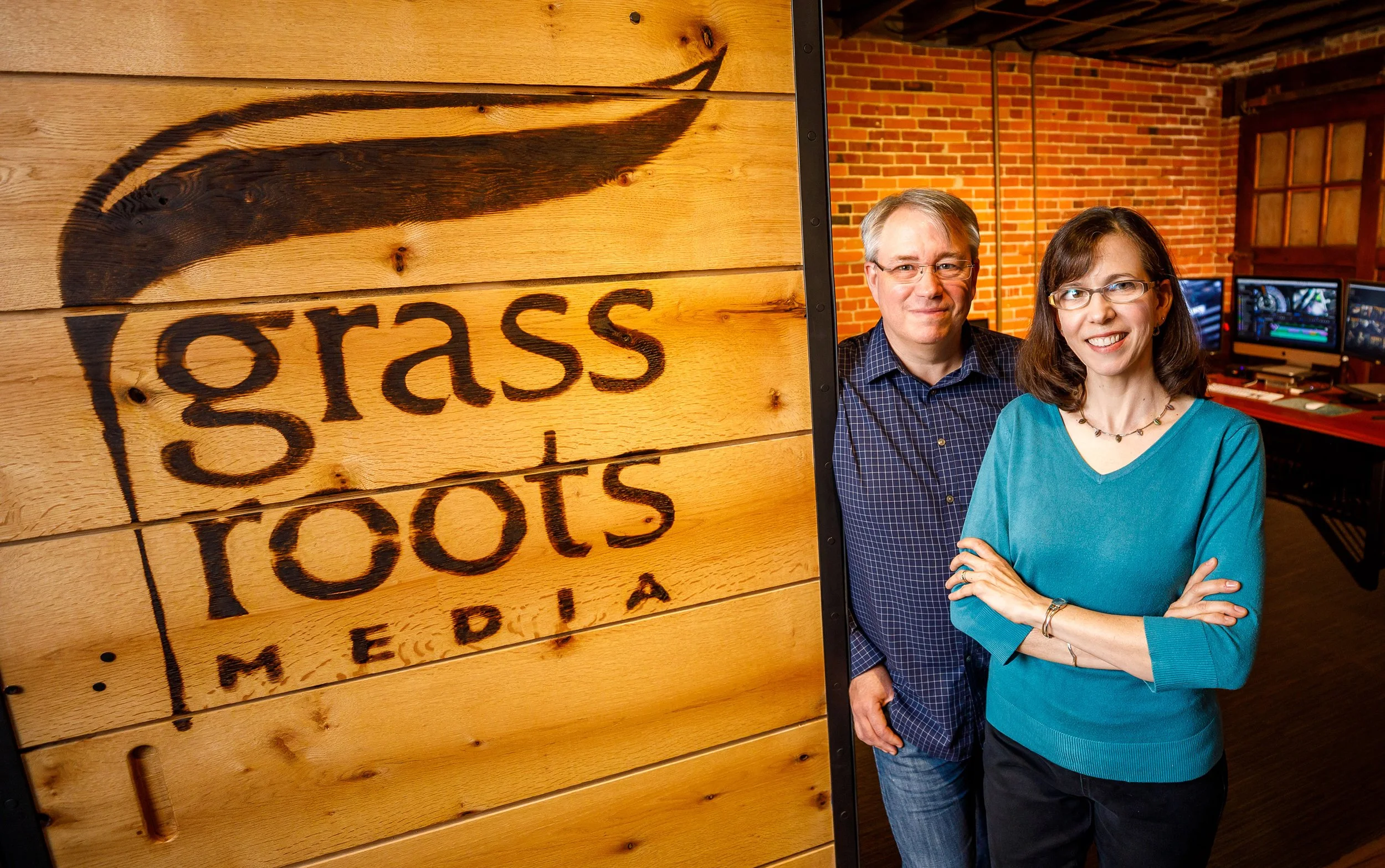 Two people standing in an office with a wooden sign that reads 'grass roots media'.