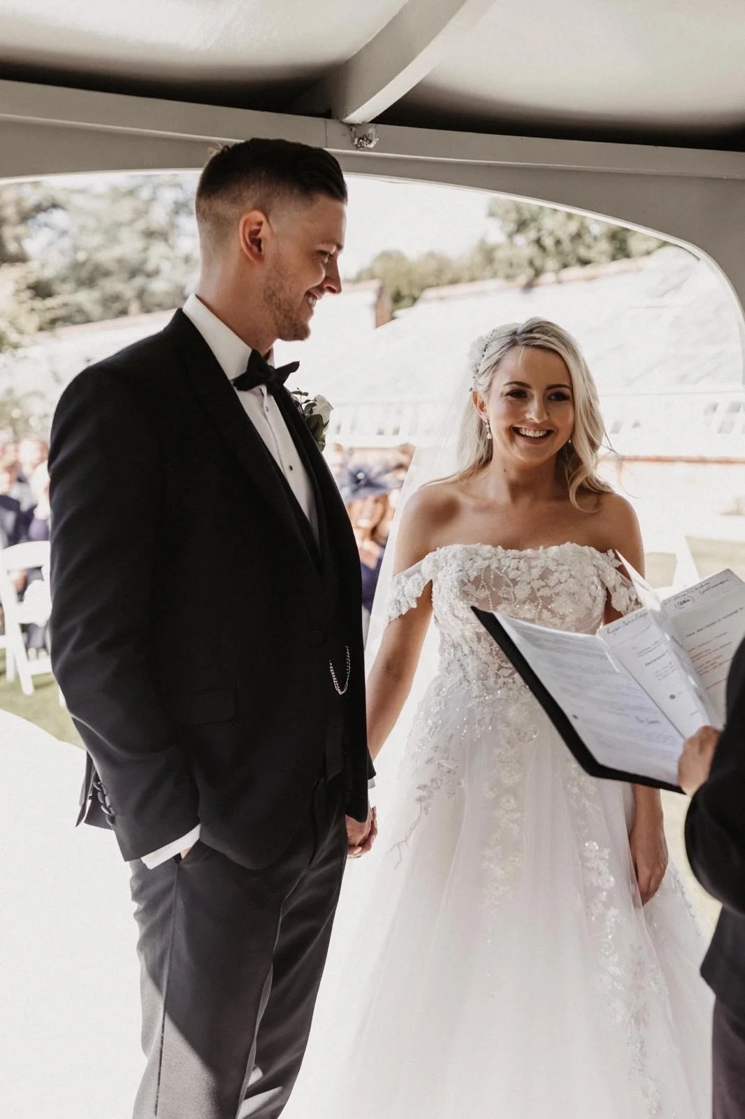 A bride and groom sharing their wedding vows during a ceremony, with an officiant holding a book in front of them.
