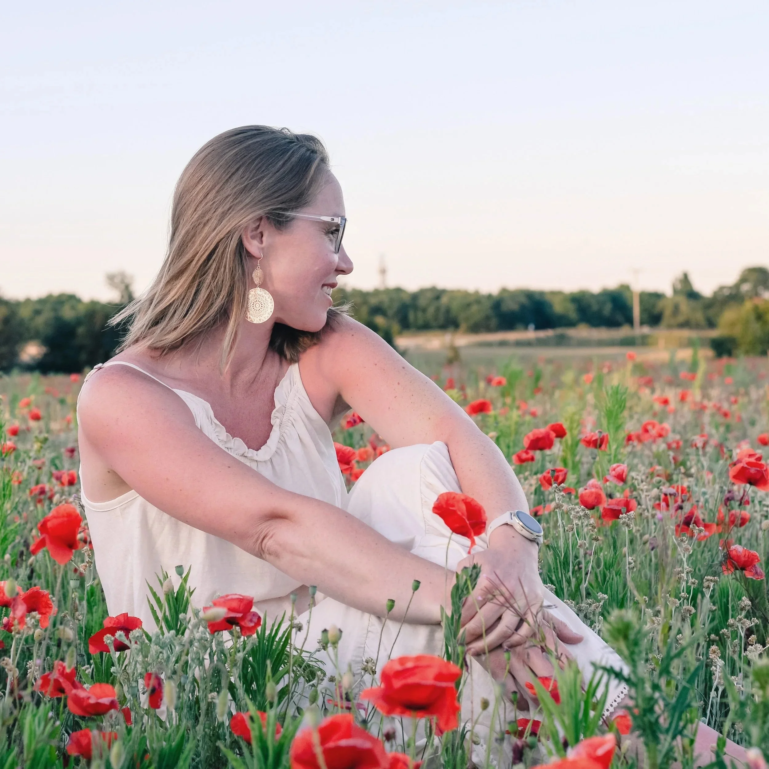 Sarah Keen sitting in a field of poppies with a big smile on her face
