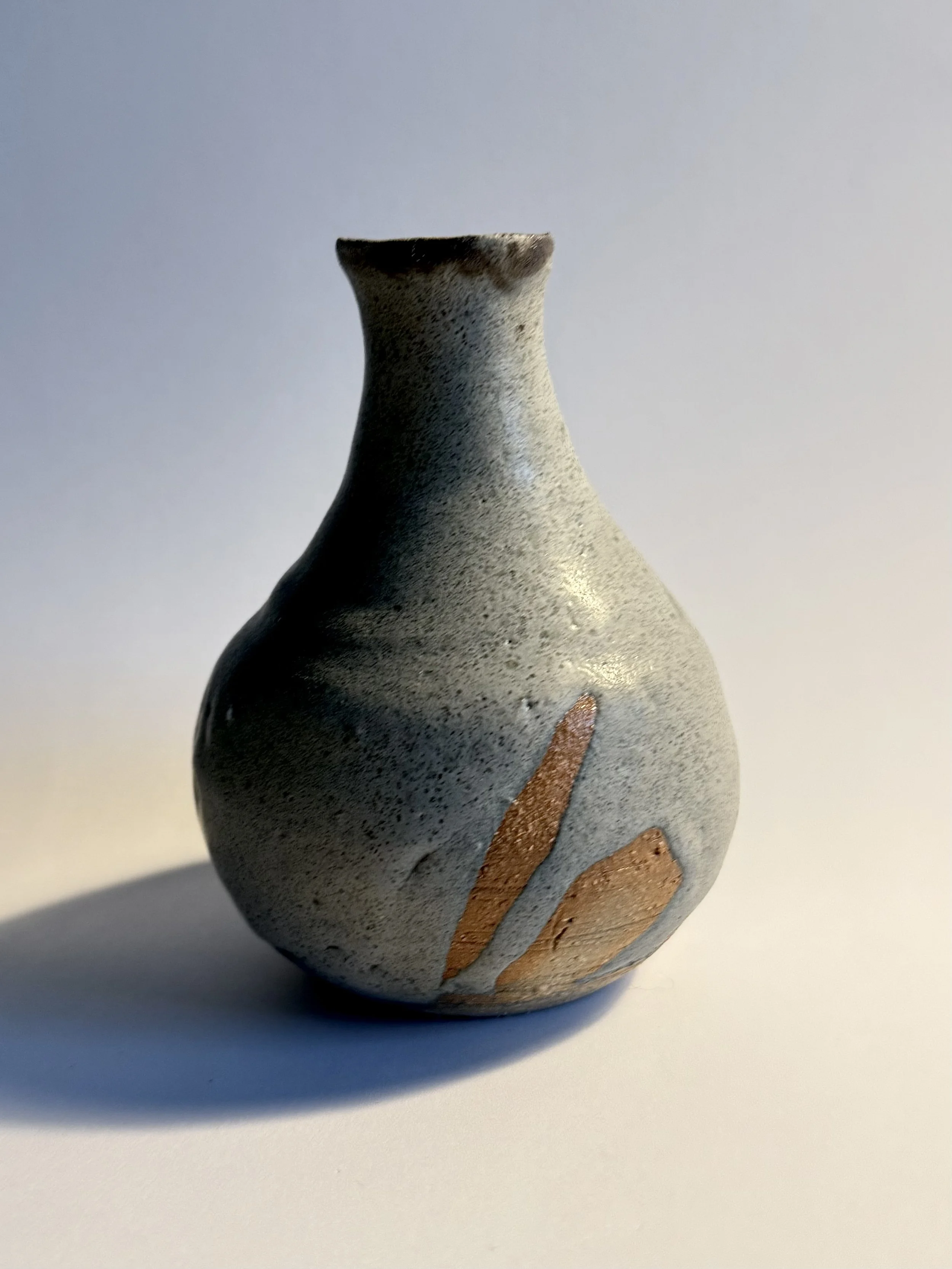 A small, round ceramic vase with a narrow neck, featuring a textured gray surface and decorative brownish-orange accents.