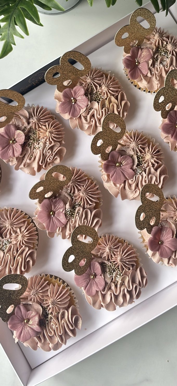 Box of cupcakes decorated with pink frosting, edible flowers, and a number '8' topper.