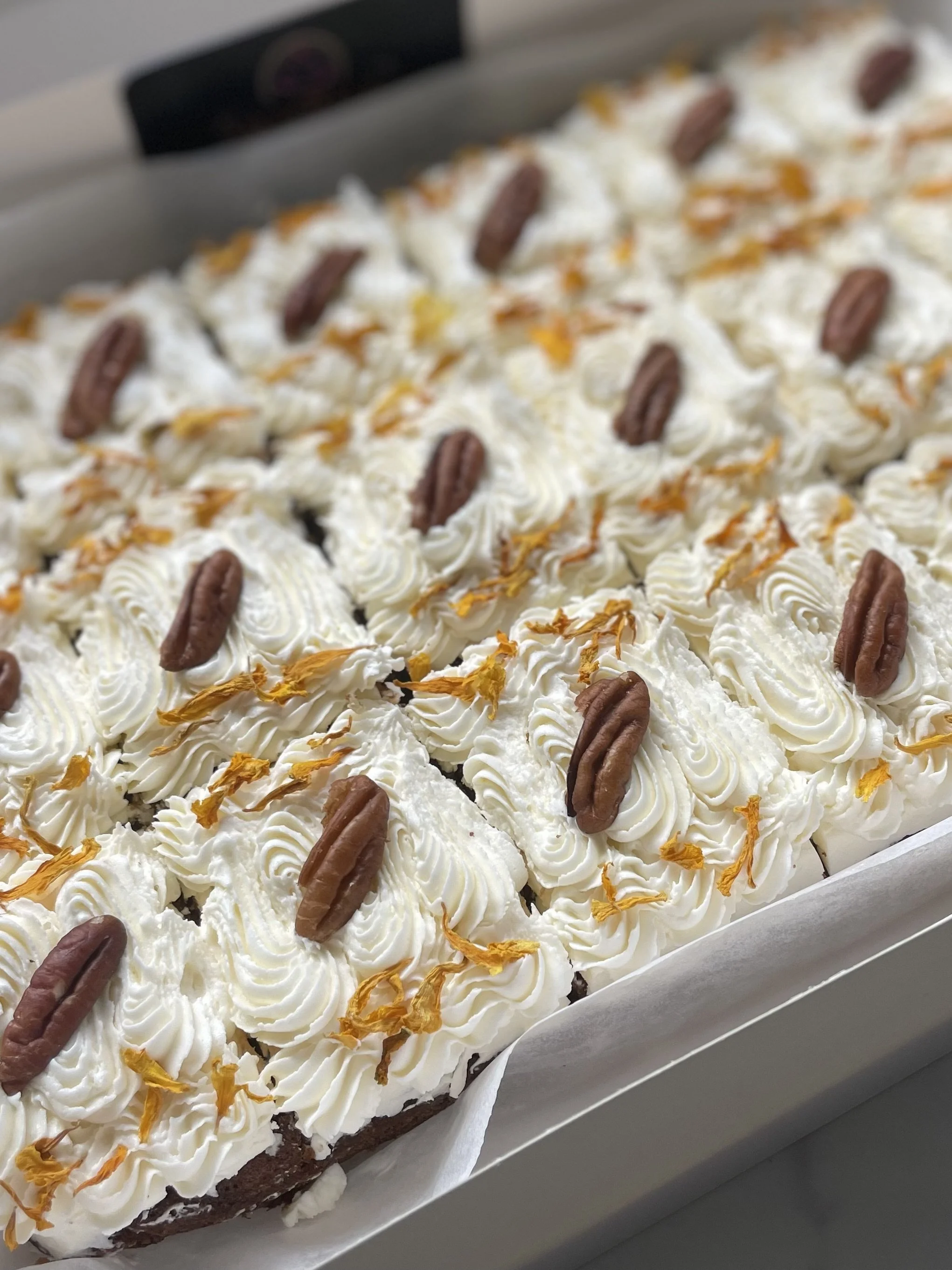 A tray of brownies decorated with swirls of white frosting, pecan halves, and orange zest.
