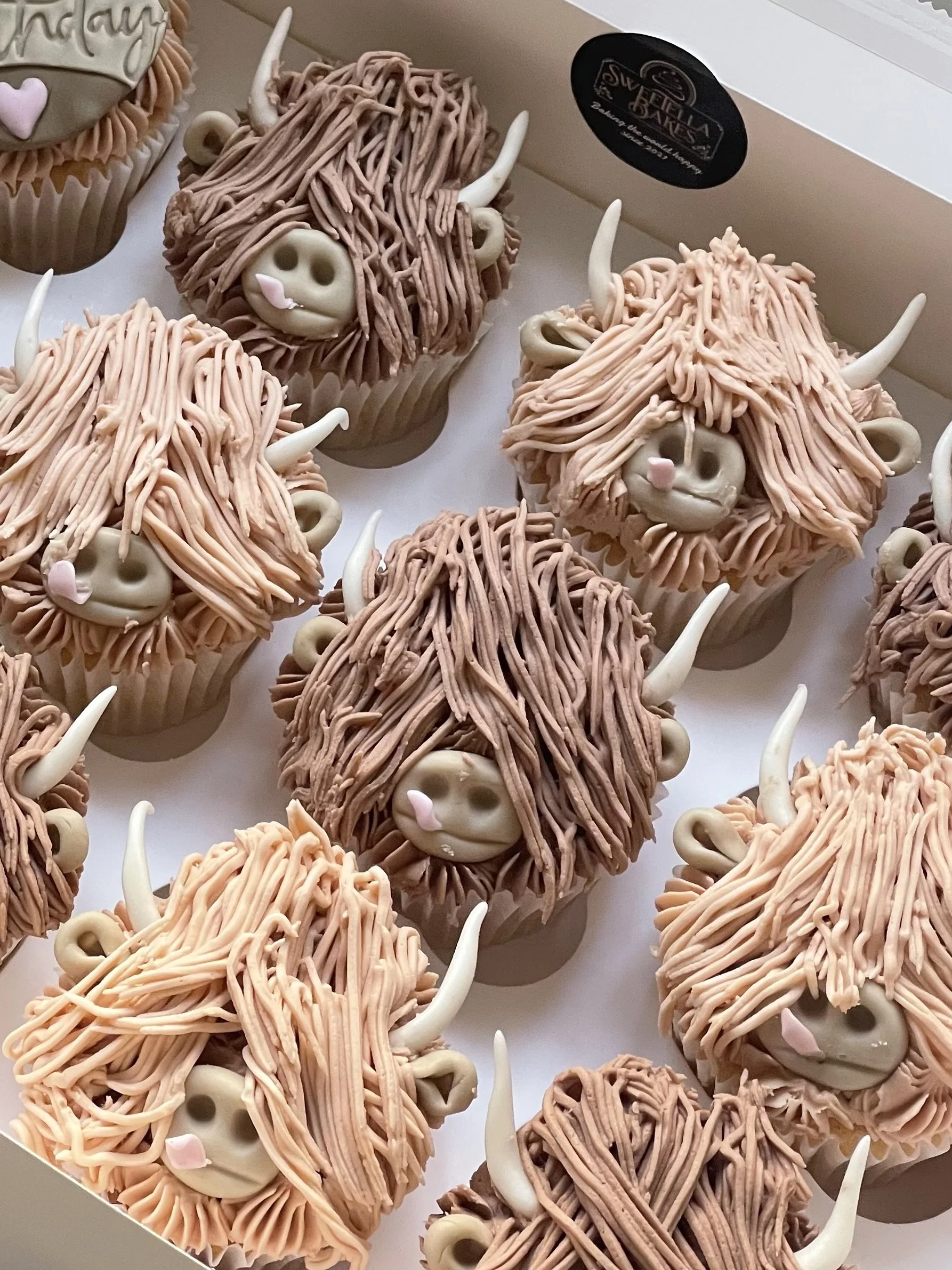 Cupcakes decorated to look like cuddly yak faces with long, textured, light brown and pinkish fur, small ears, horns, and smiling faces.