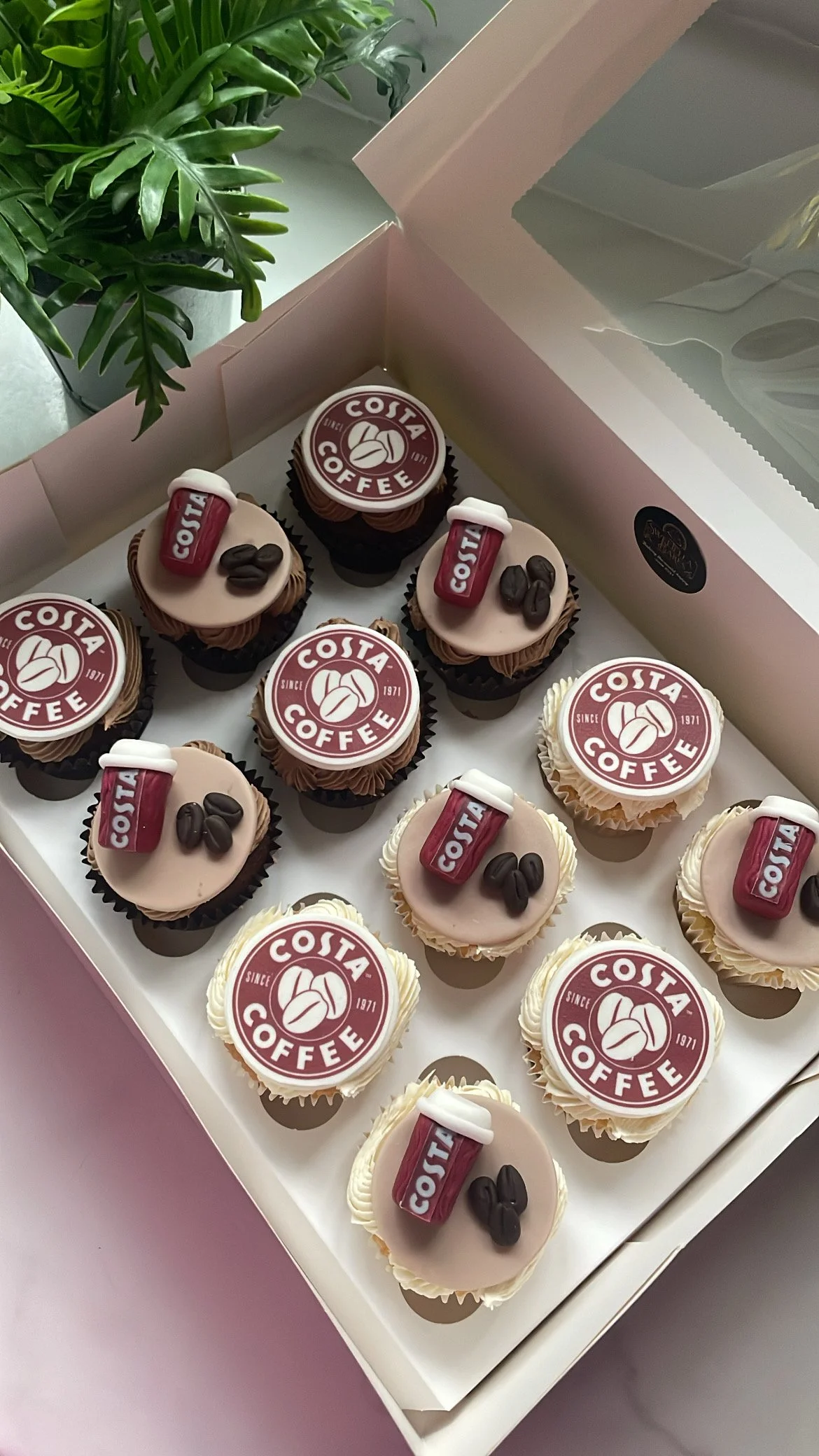 Cupcakes decorated with logos and symbols of Costa Coffee, featuring the brand name, coffee beans, and a coffee cup.