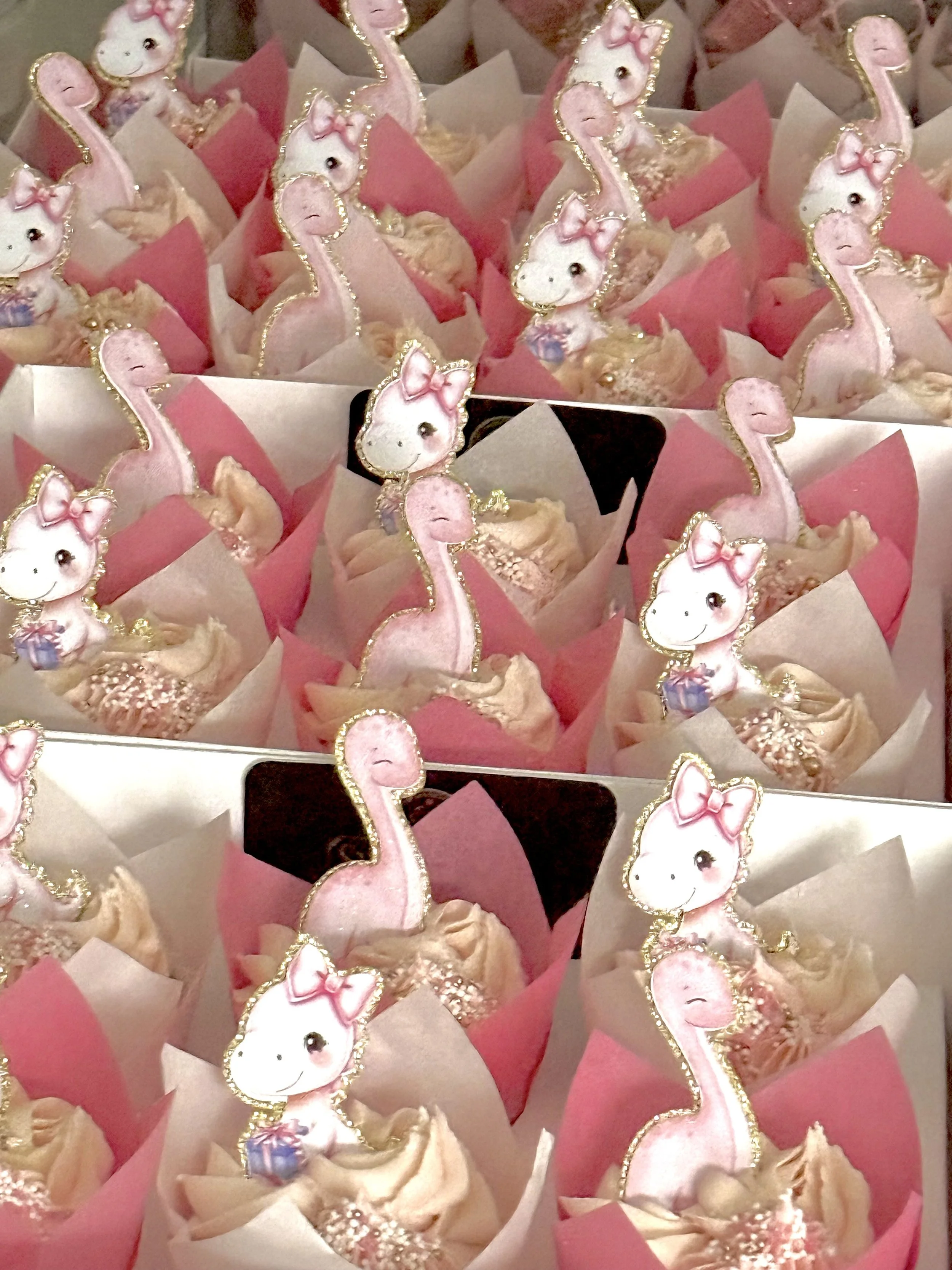 Cupcakes decorated with cute animal toppers, pink and white paper wrappers, some with sprinkles.