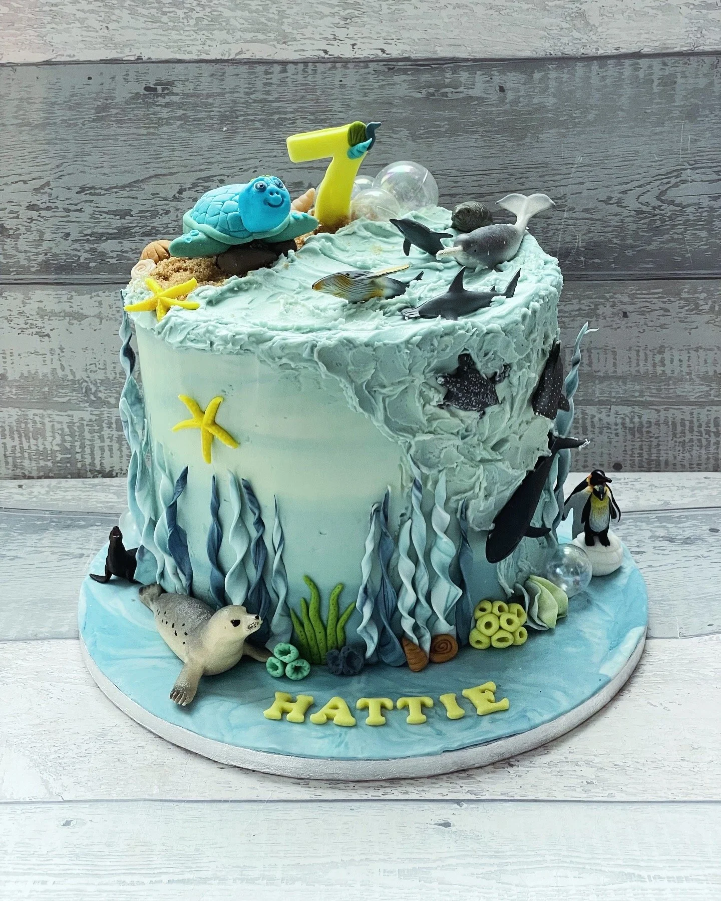A nautical-themed cake decorated with ocean creatures, starfish, and seaweed, with the name 'HATTIE' on the base.
