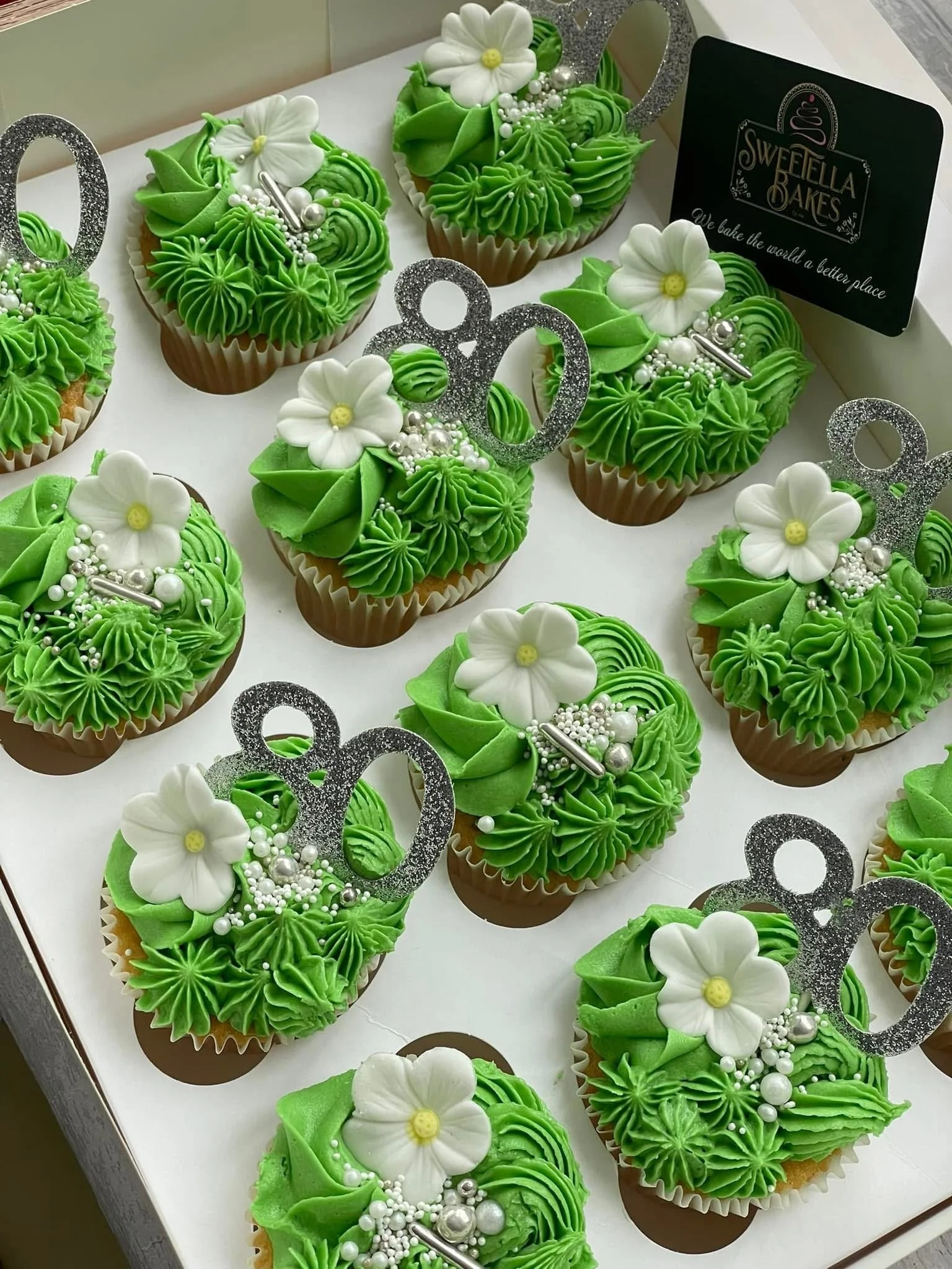 Cake cupcakes decorated for a celebration with green frosting, white flowers, and silver decorations.