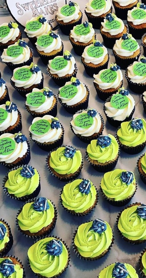 Cupcakes with green and white swirled frosting topped with blue flowers, arranged in rows for a celebration.