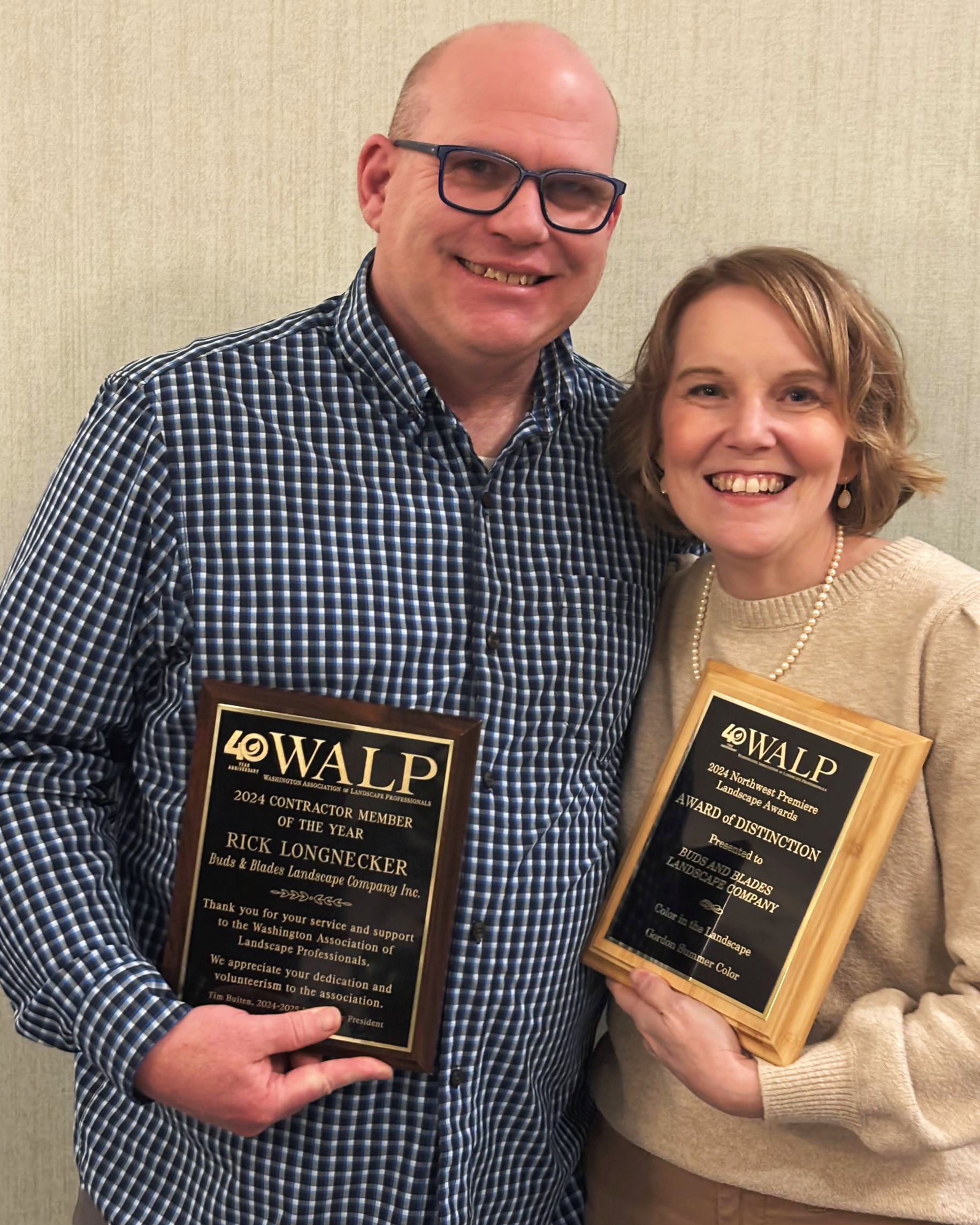 Rick and Nicole Longnecker smiling while holding awards, standing against a beige wall.