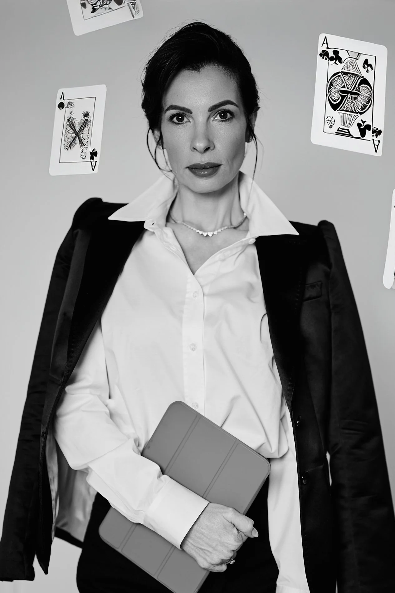 A woman in business attire holding a tablet, with playing cards floating around her, against a plain background.