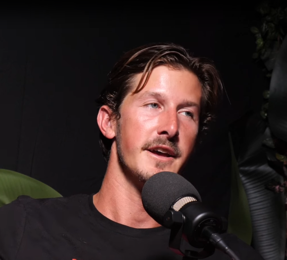 A young man with brown hair and facial hair speaking into a microphone.