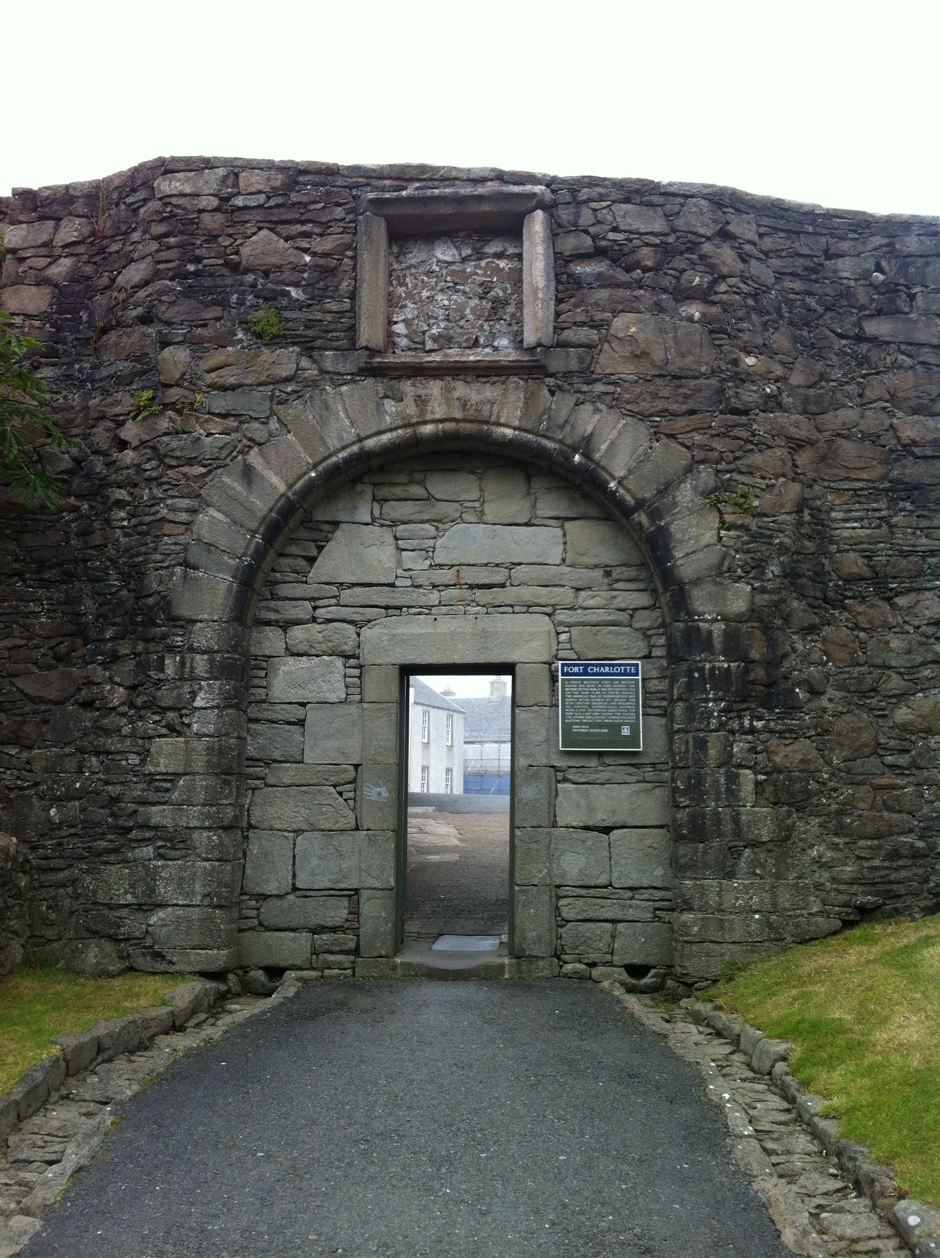 Historical stone fortress wall with an arched doorway and a sign that reads 'Fort Charlotte' in front of a city street.