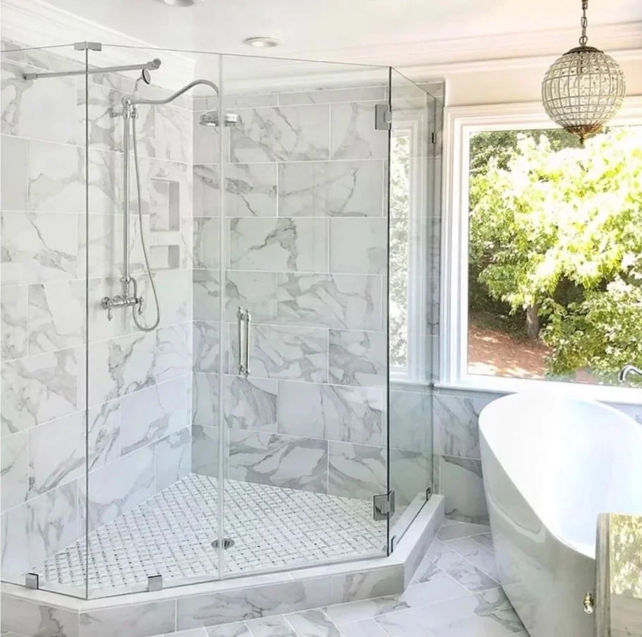 Bathroom with a glass-enclosed shower and a white bathtub near a large window with trees outside.