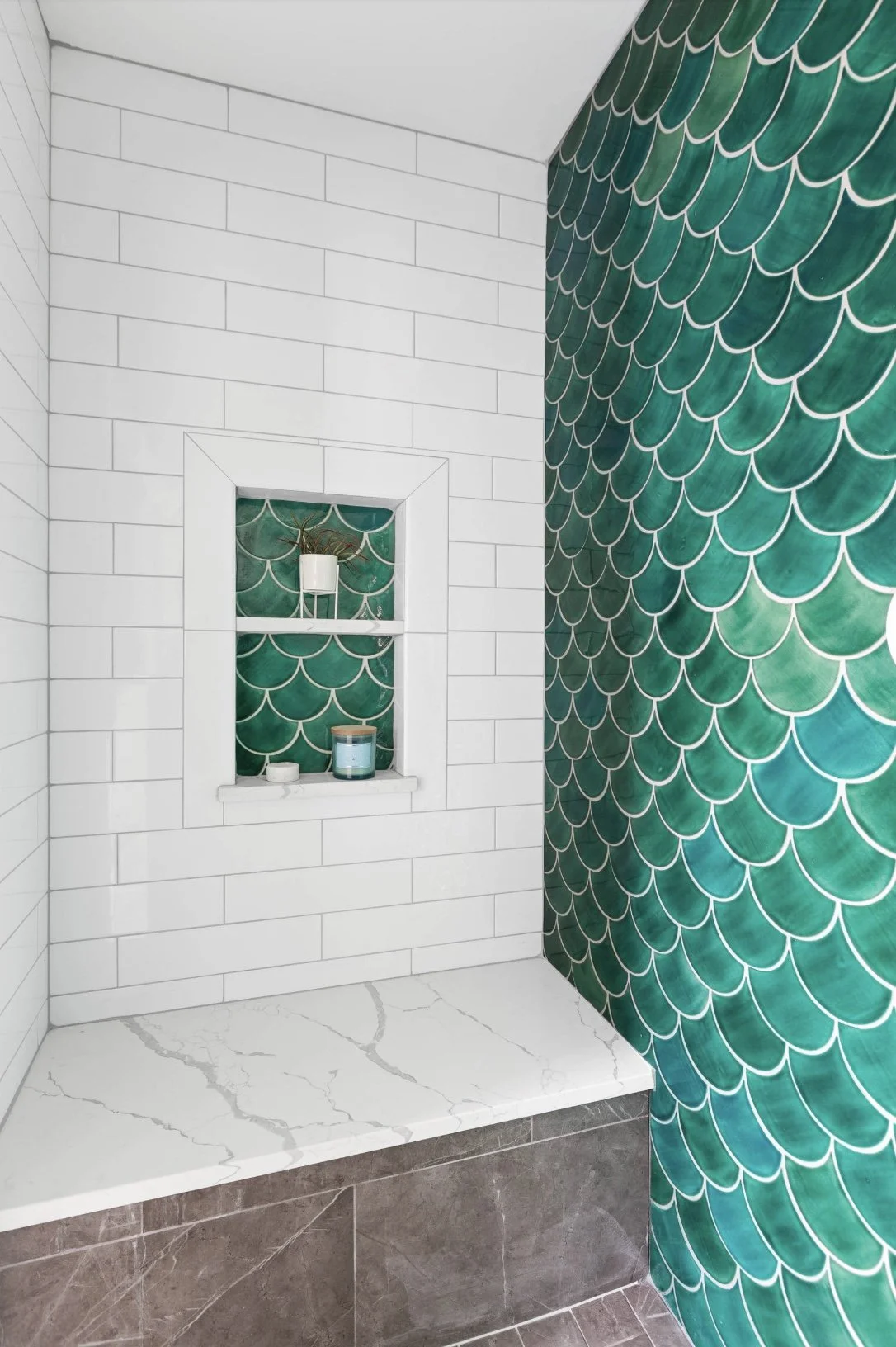 Decorative tiled shower with a shelf and a niche featuring white subway tiles and green fish scale tiles.