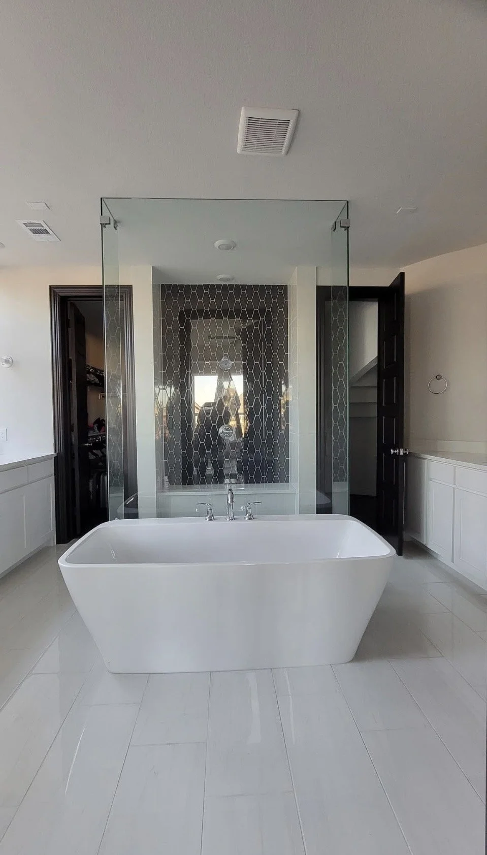 Modern bathroom with a freestanding white bathtub, glass shower enclosure with black hexagonal tiles, and white wall paneling.
