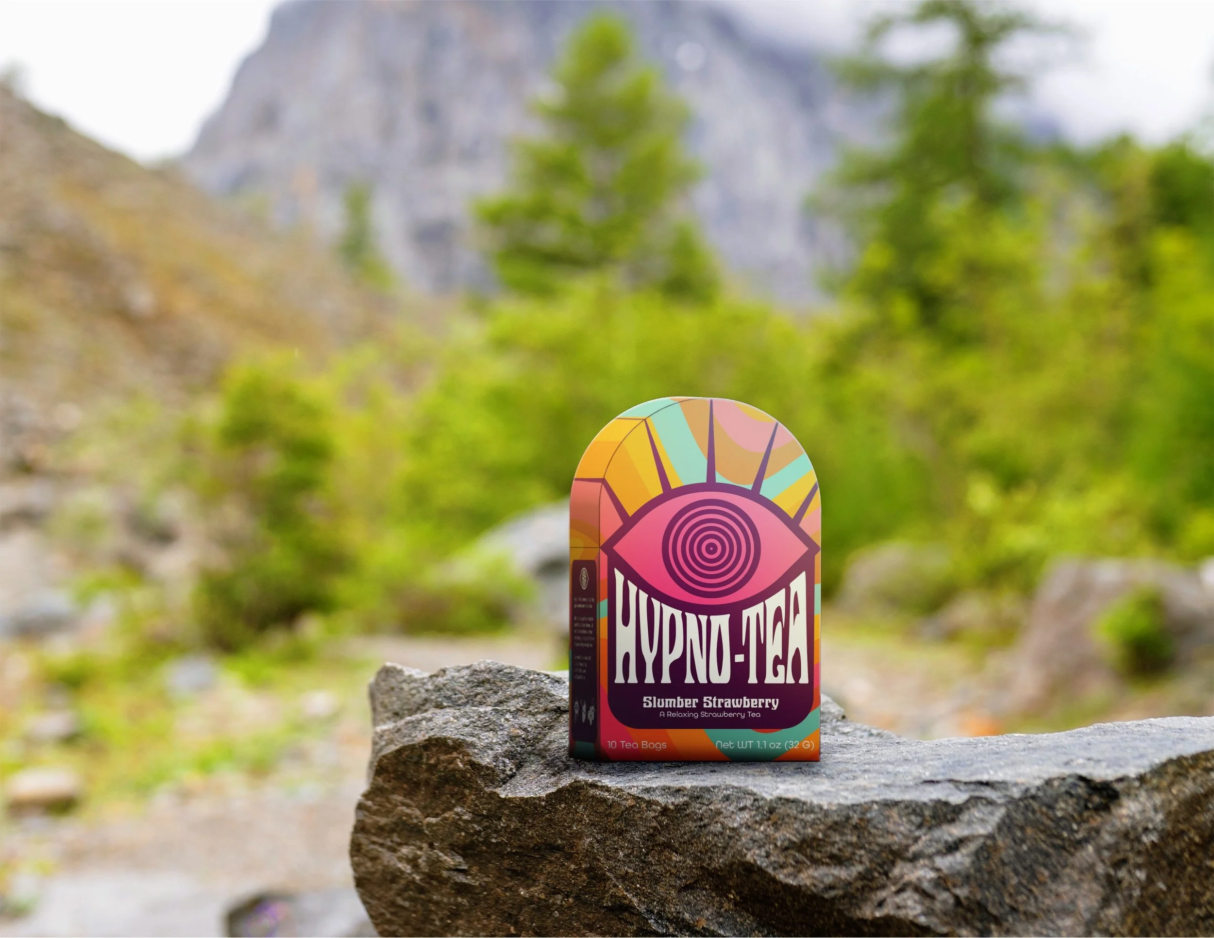 Colorful box of strawberry flavored tea sitting on a rock outdoors with green trees and mountains in the background.