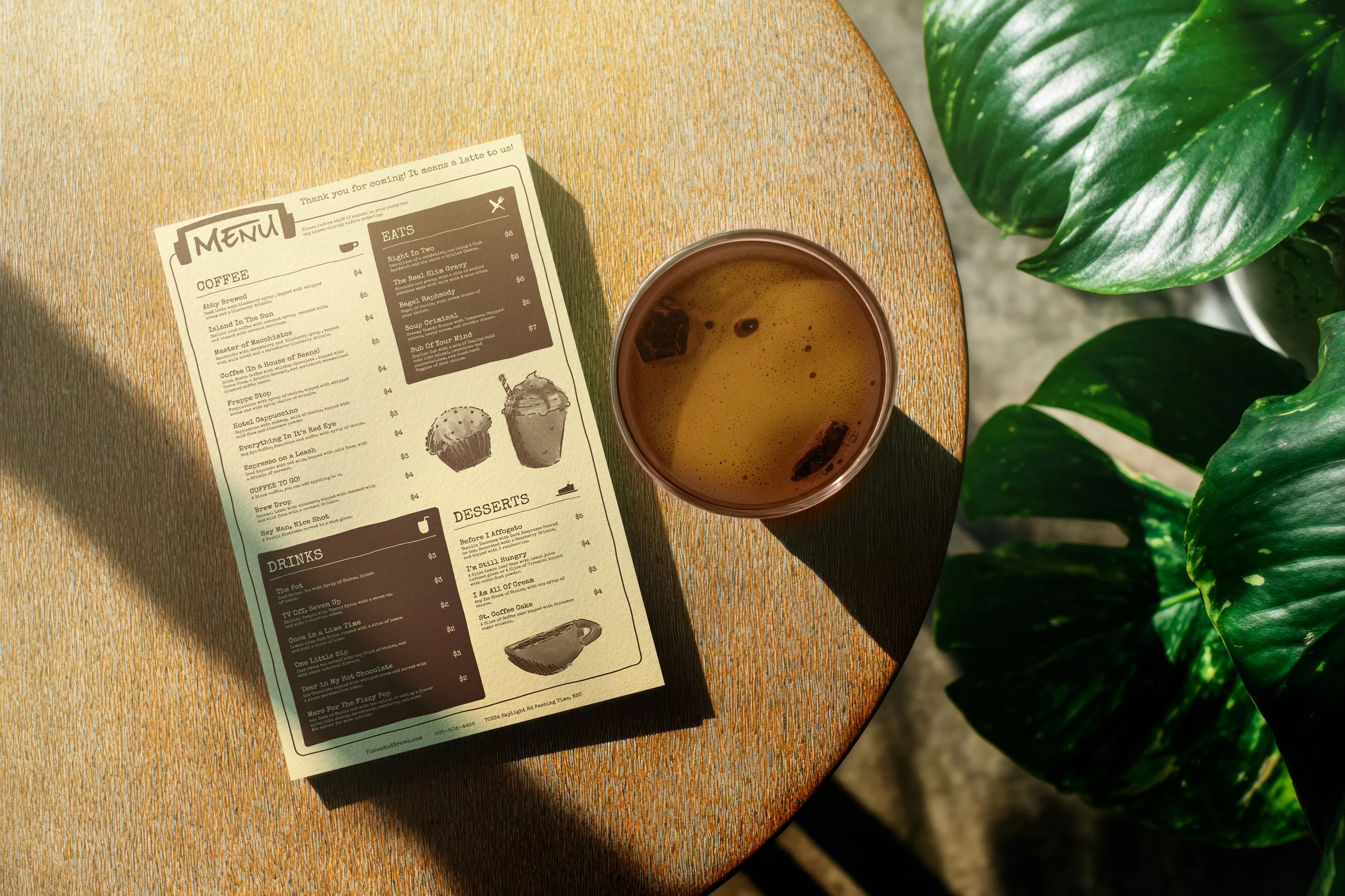 A coffee menu and a cup of coffee on a wooden table with a green leafy plant nearby.